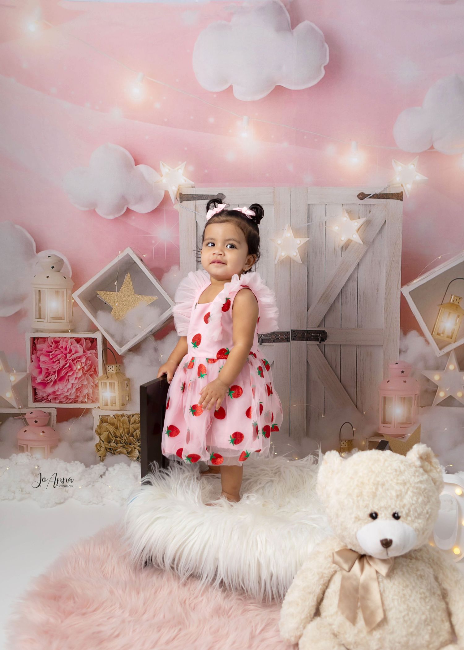 Baby girl standing on a baby bed in front of a pink cloud themed set