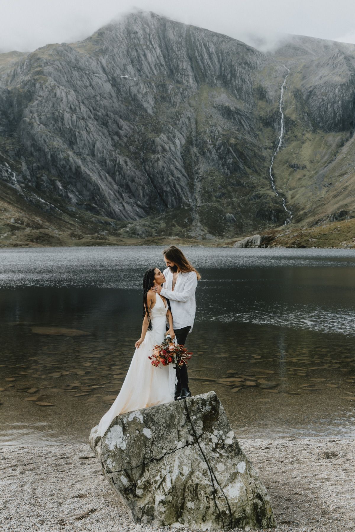 Couple embracing during an intimate elopement in North Wales with mountains in the background, photographed in a natural documentary style.