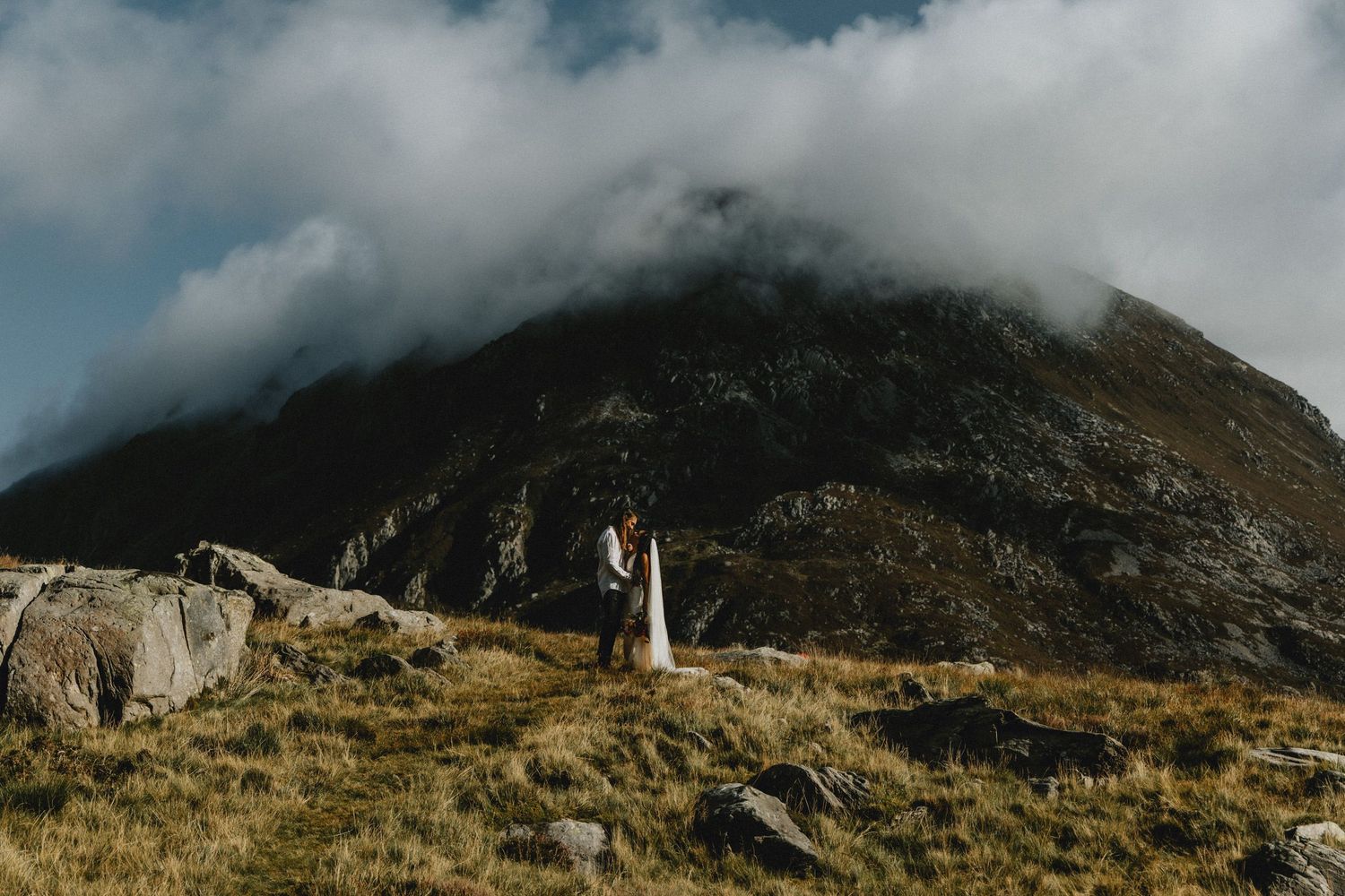 Couple embracing during an intimate elopement in North Wales with mountains in the background, photographed in a natural documentary style.