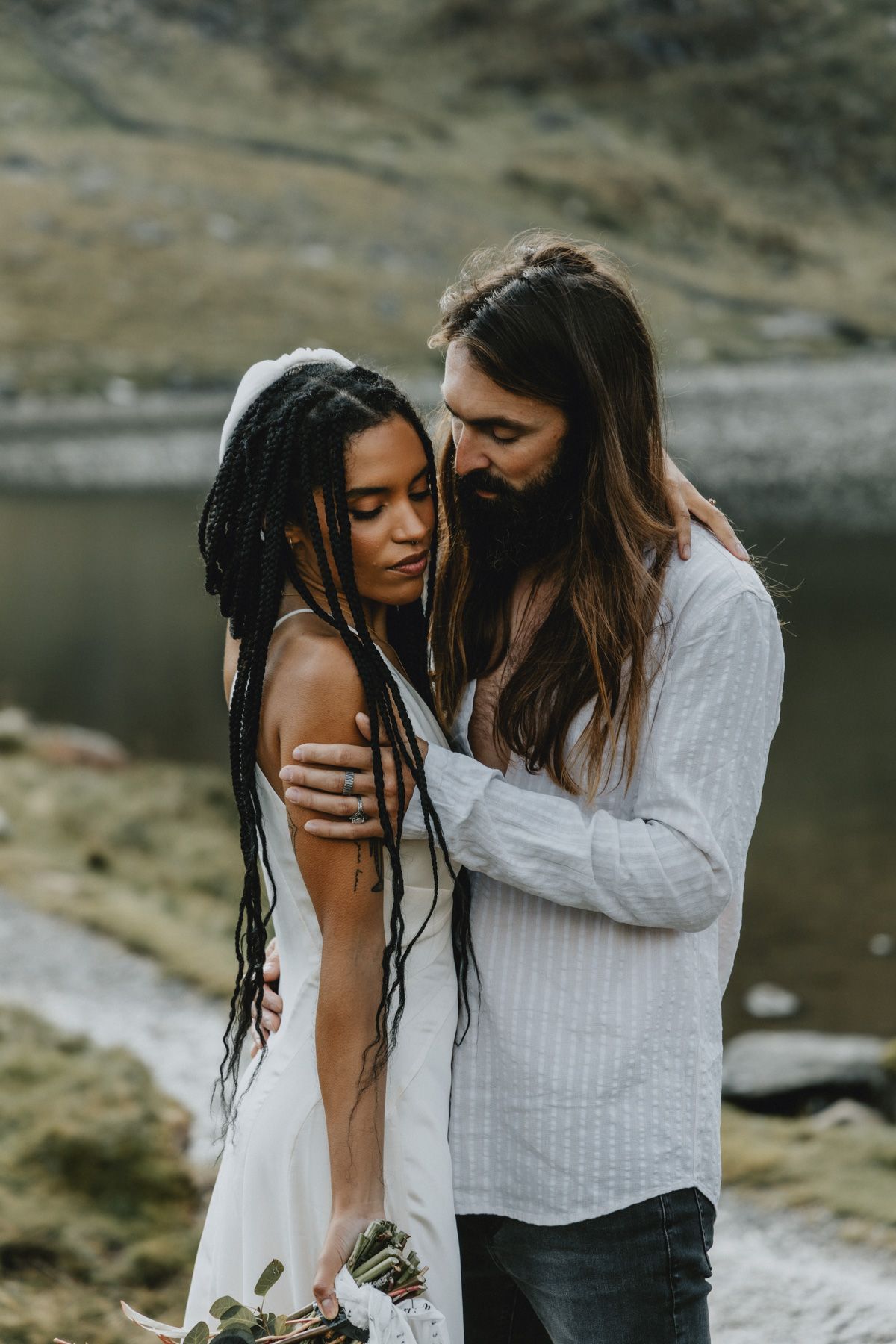 Couple embracing during an intimate elopement in North Wales with mountains in the background, photographed in a natural documentary style.