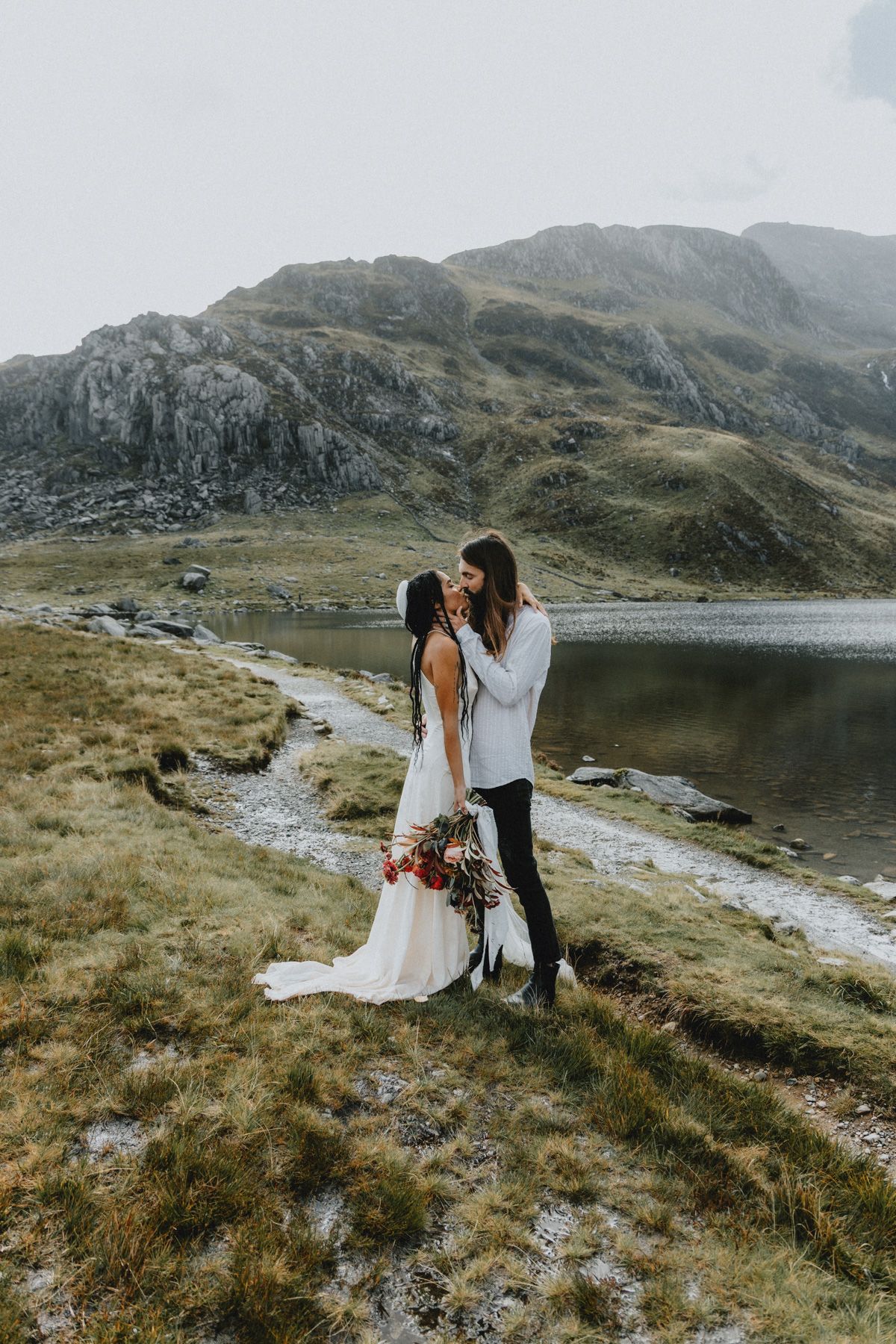 Couple embracing during an intimate elopement in North Wales with mountains in the background, photographed in a natural documentary style.