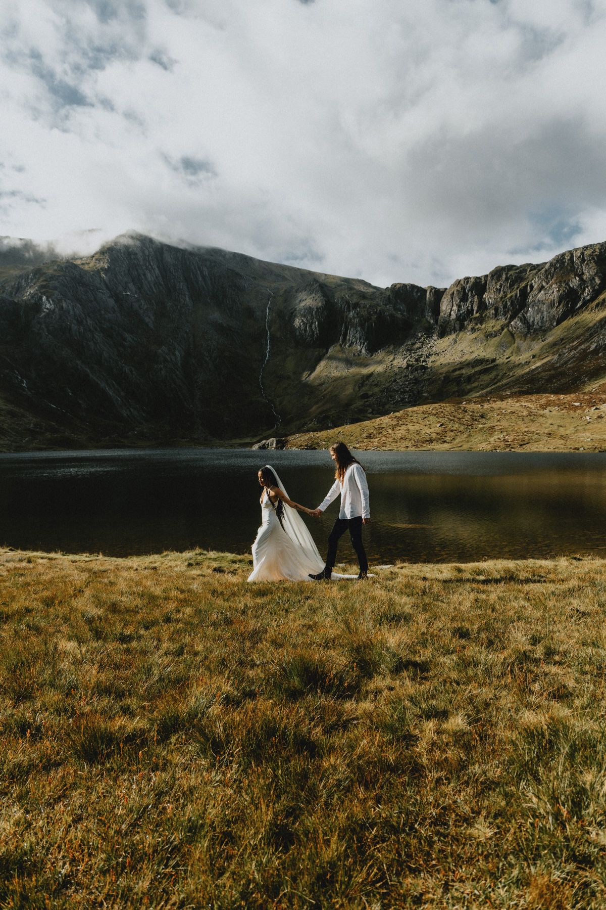 Couple embracing during an intimate elopement in North Wales with mountains in the background, photographed in a natural documentary style.