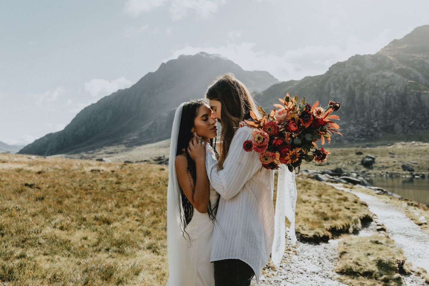 Couple embracing during an intimate elopement in North Wales with mountains in the background, photographed in a natural documentary style.