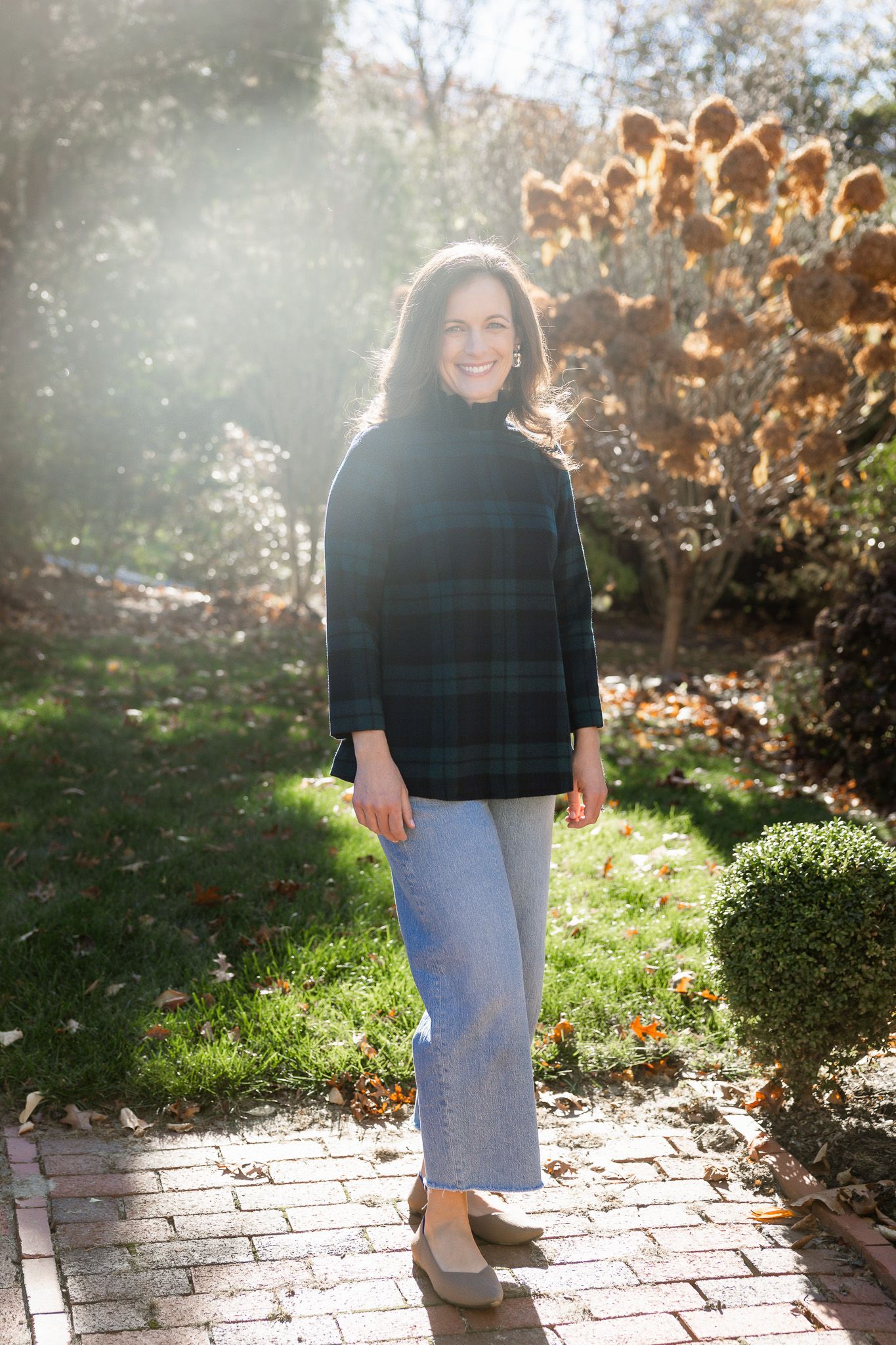 Person wearing a black sweater and jeans walks on a brick pathway in dappled sunlight.