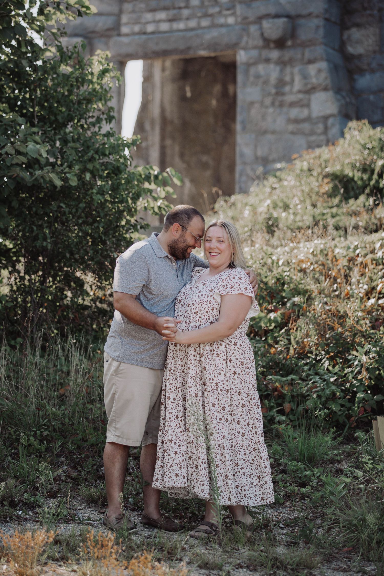 A couple sharing tender moments near a stone wall surrounded by garden foliage.