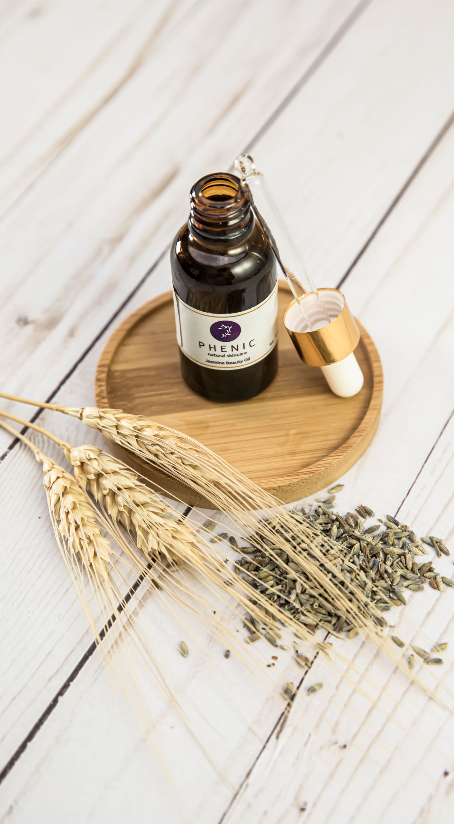 Essential oil bottle on wooden tray with dried wheat and lavender stems.