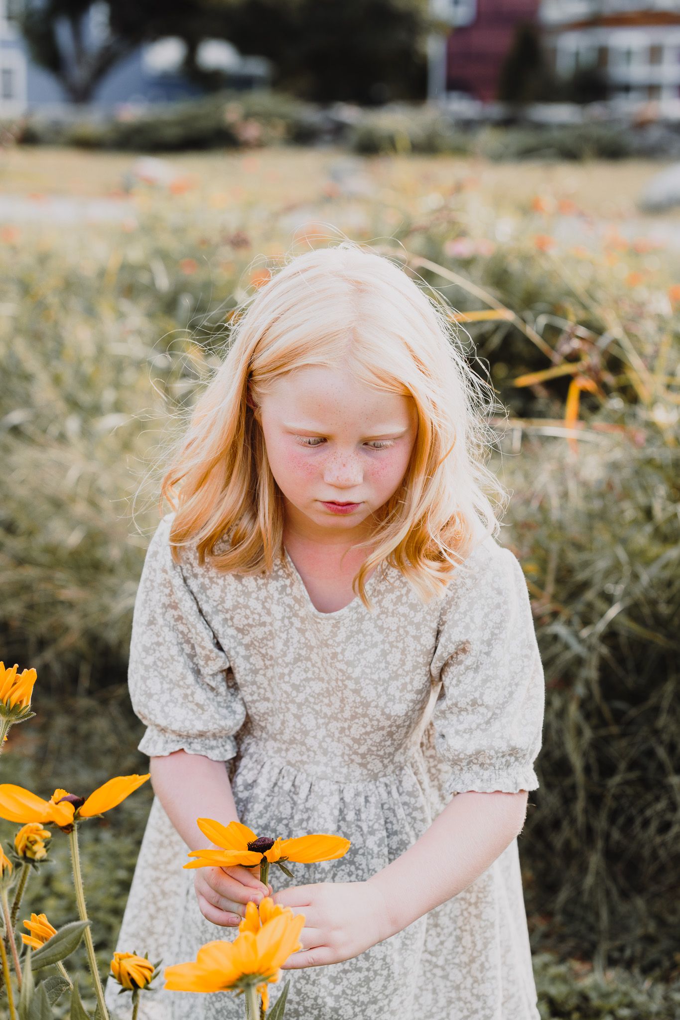 Child in vintage dress gently touching yellow flowers in a garden.
