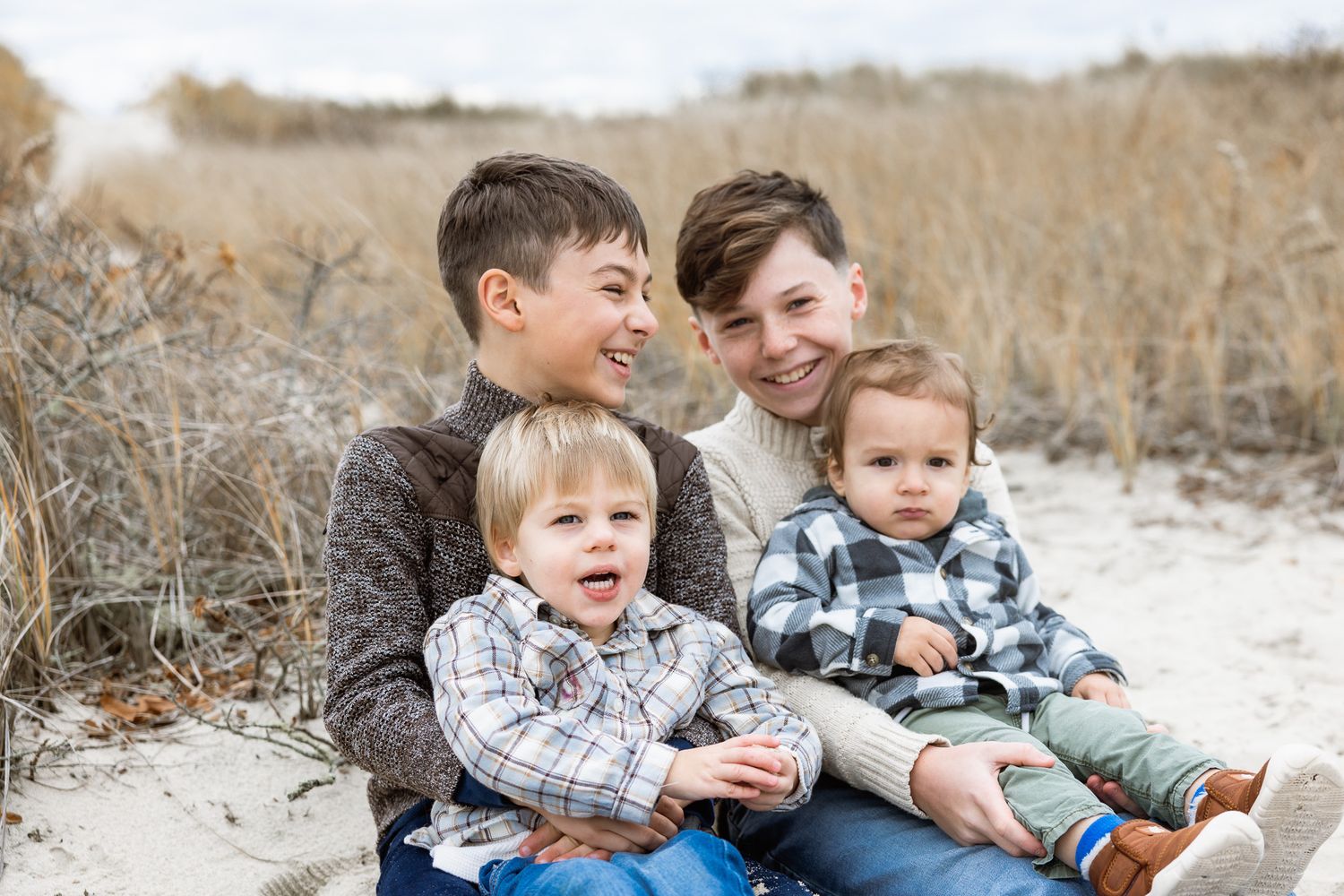 Children sharing playful moments on sandy ground during family photoshoot.