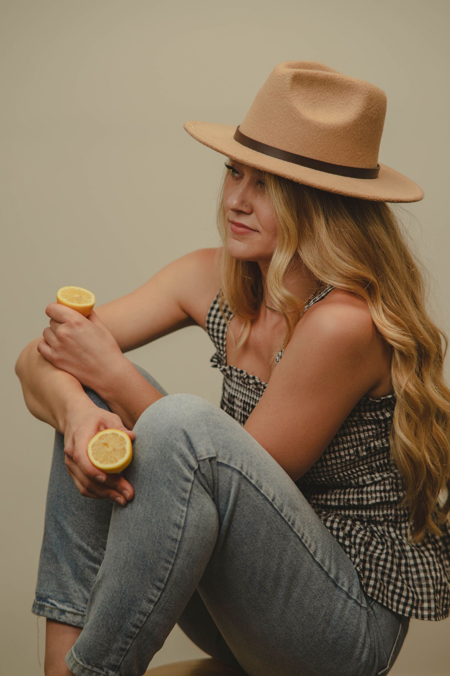 Stylish portrait series with tan fedora, gingham top, and jeans holding a lemon.