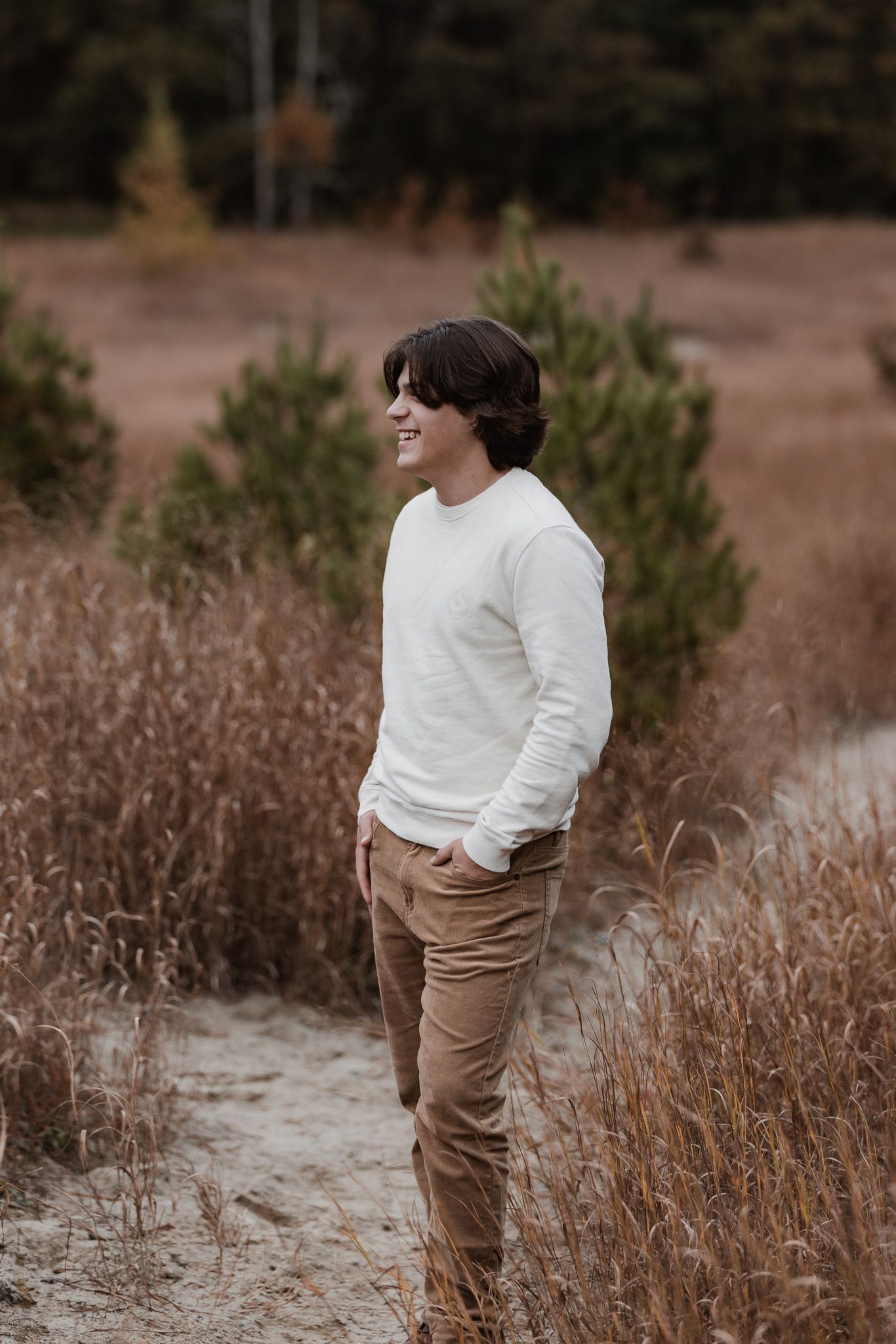 Figure in white sweater and khaki pants poses among dried winter grasses.