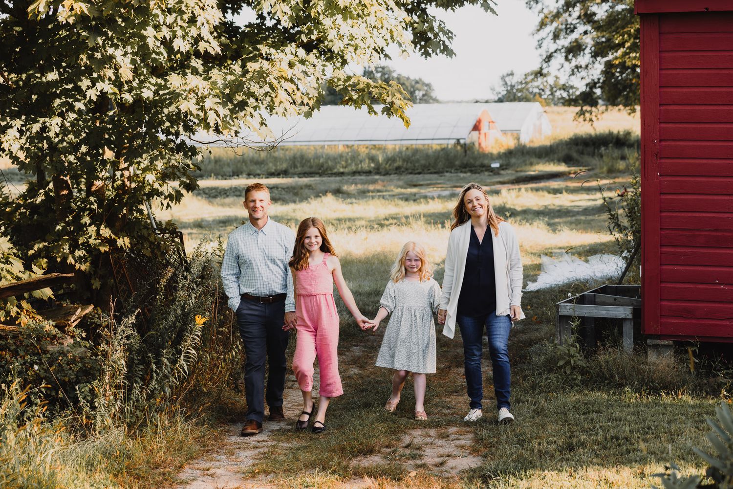 Family walking together along a red barn in golden evening sunlight.