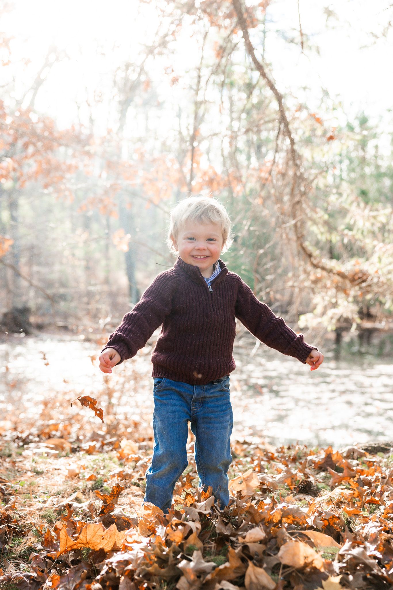 Child running through scattered fall leaves wearing blue jeans and dark sweater.