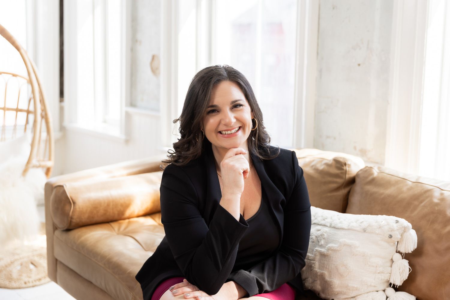Person in black blazer relaxes on a light-colored couch in a bright, airy room.