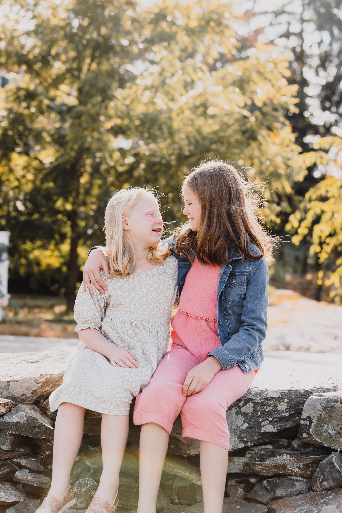 Children sitting together on stone wall sharing sweet moments at sunset.
