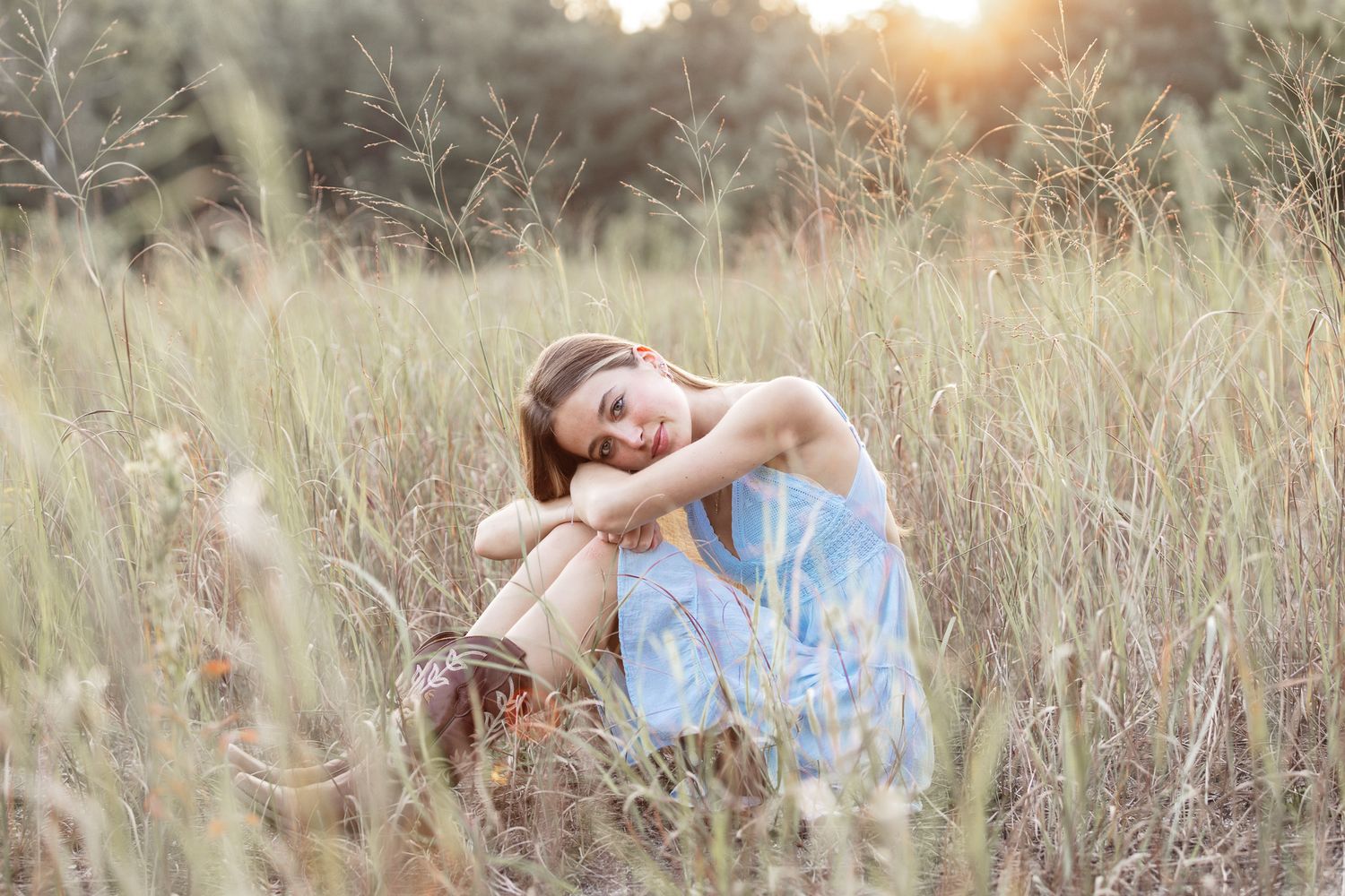 Person in blue dress lounges in golden field during sunset photo session.