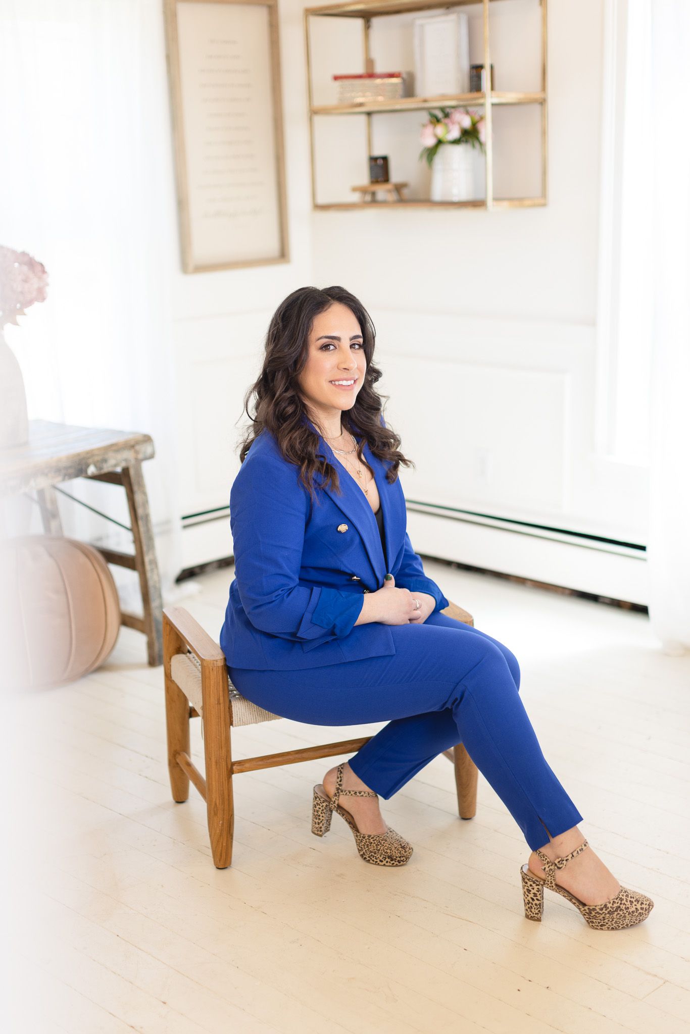 Professional fashion photoshoot featuring a royal blue pantsuit and leopard print heels in a bright white studio setting.