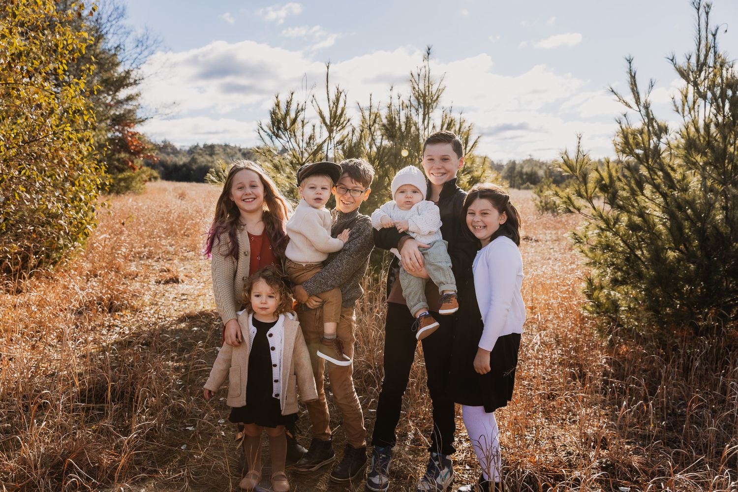 Joyful outdoor family portrait among evergreen trees in autumn landscape.