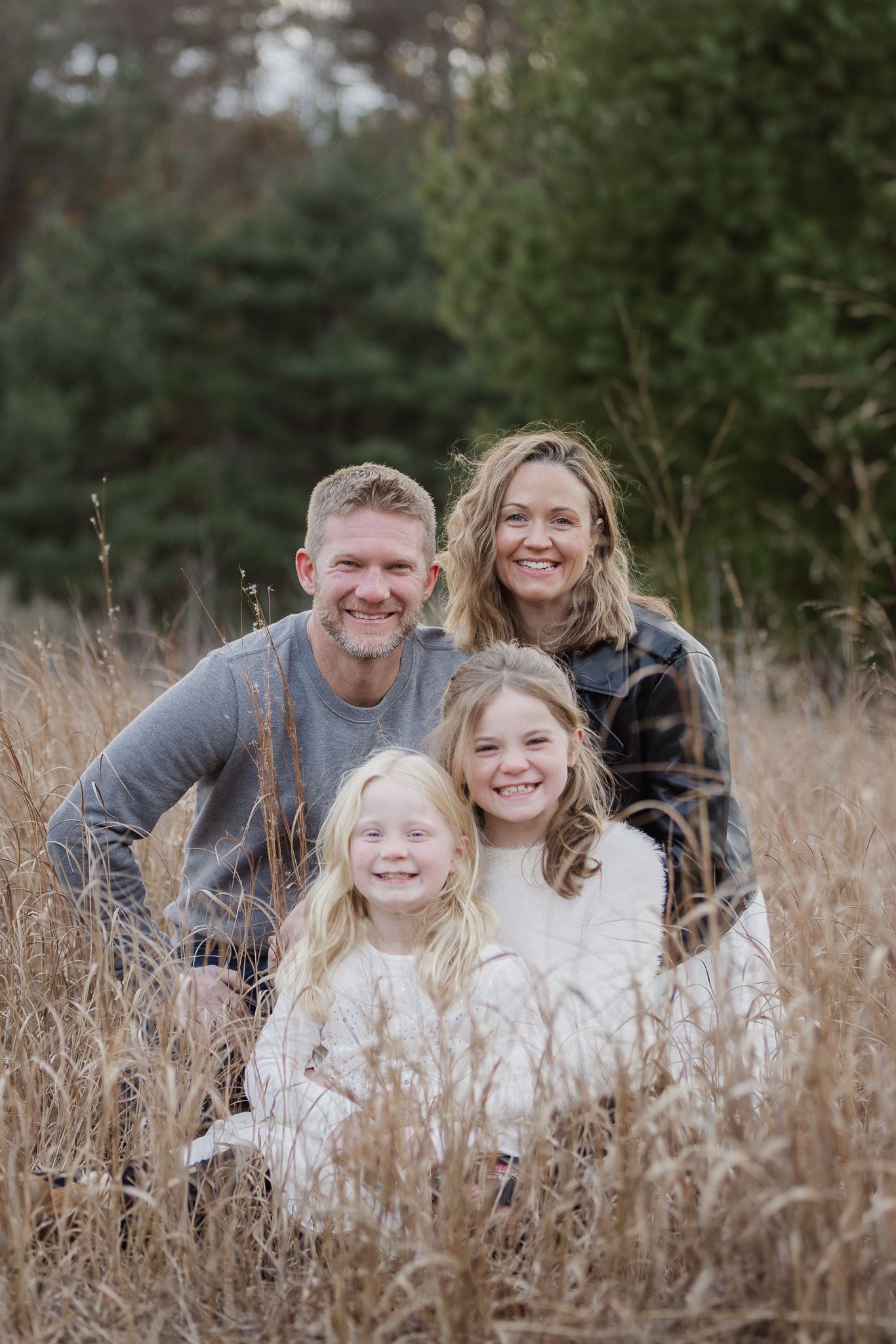 Family group sitting together in tall autumn grass field.