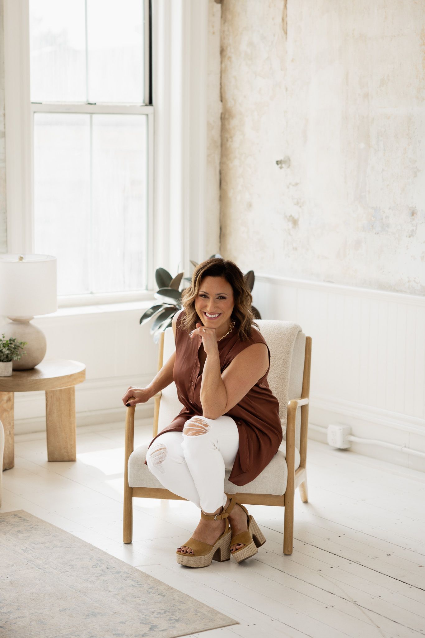 Lifestyle portraits in white studio space with brown jacket and wooden furniture.