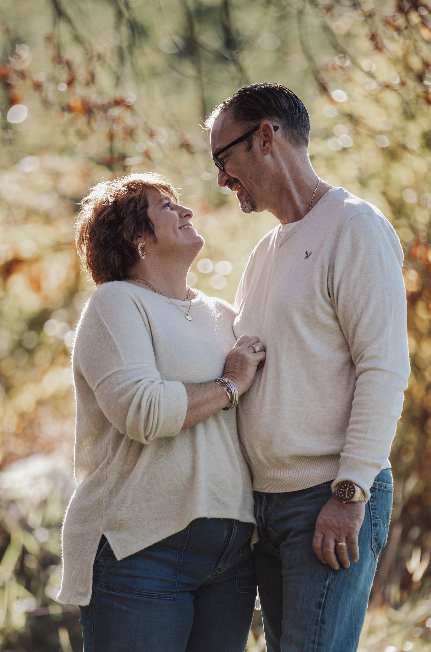 A couple wearing matching cream sweaters shares a tender moment outdoors.