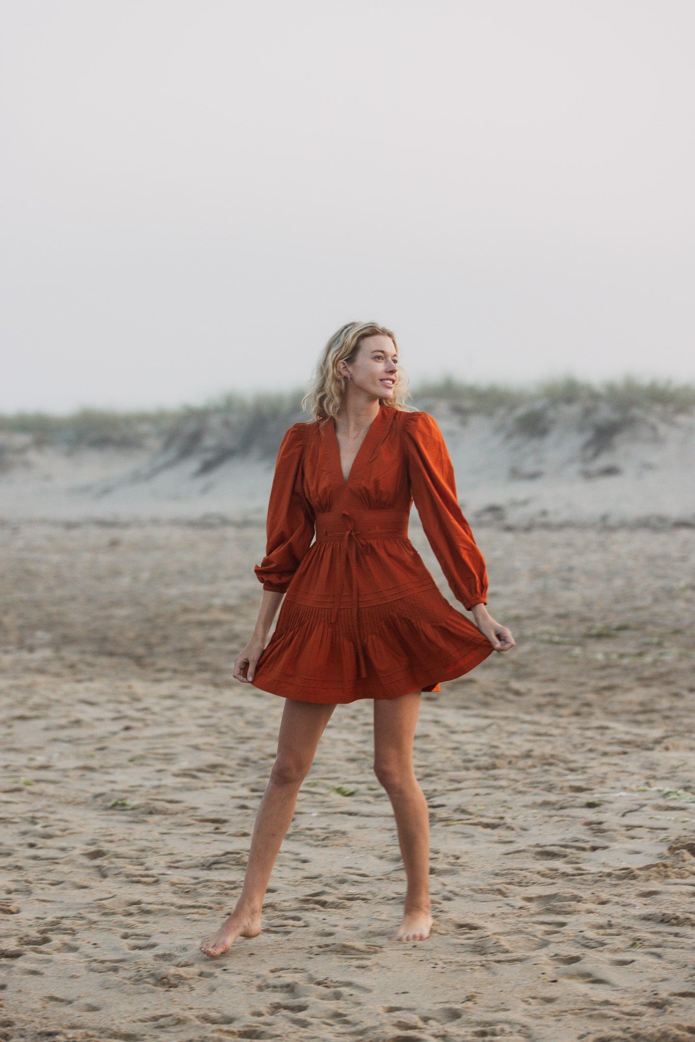 Woman in red dress twirling on sandy beach at sunset.