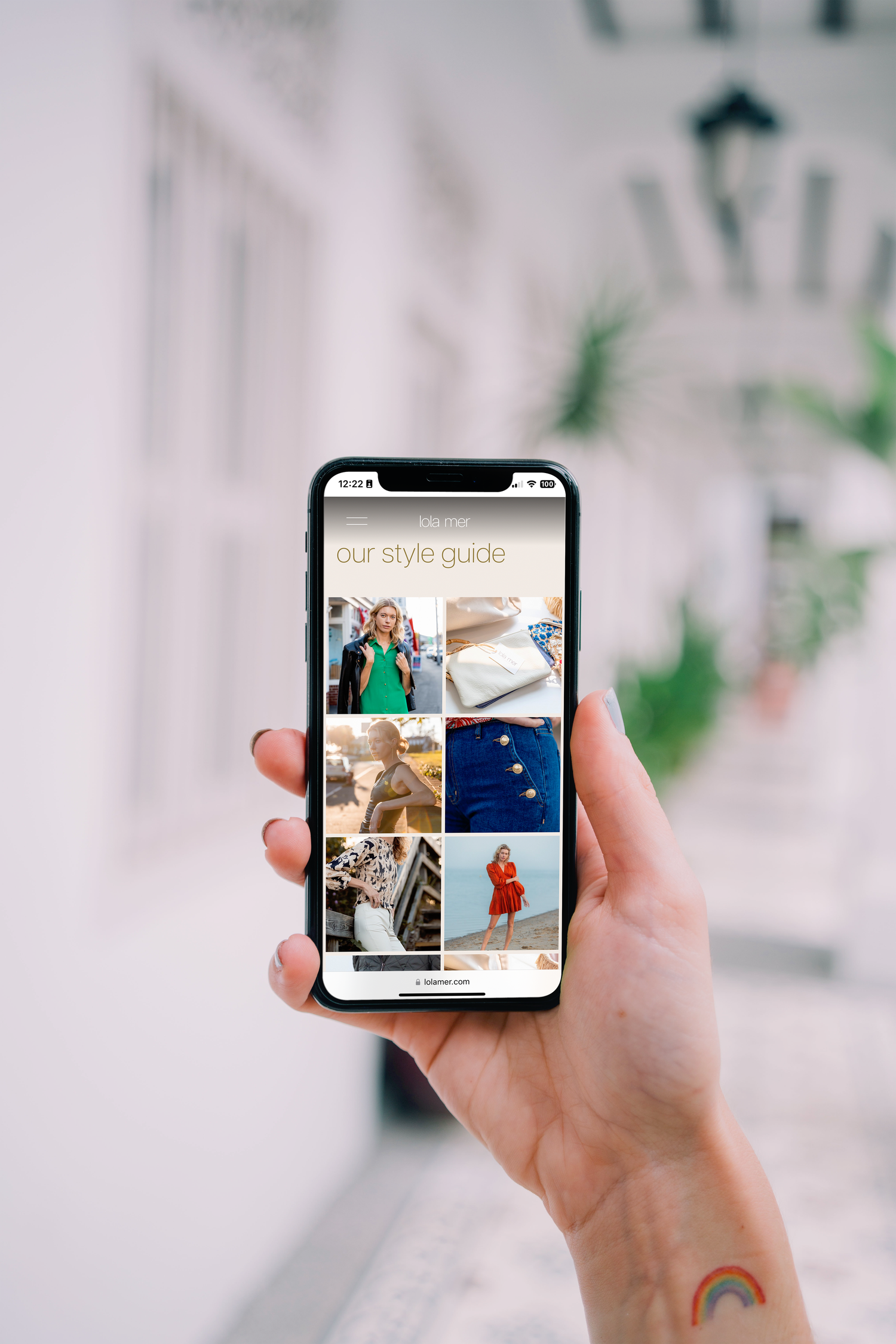 Hand holding smartphone displaying photo gallery grid with travel and lifestyle images against blurred background.