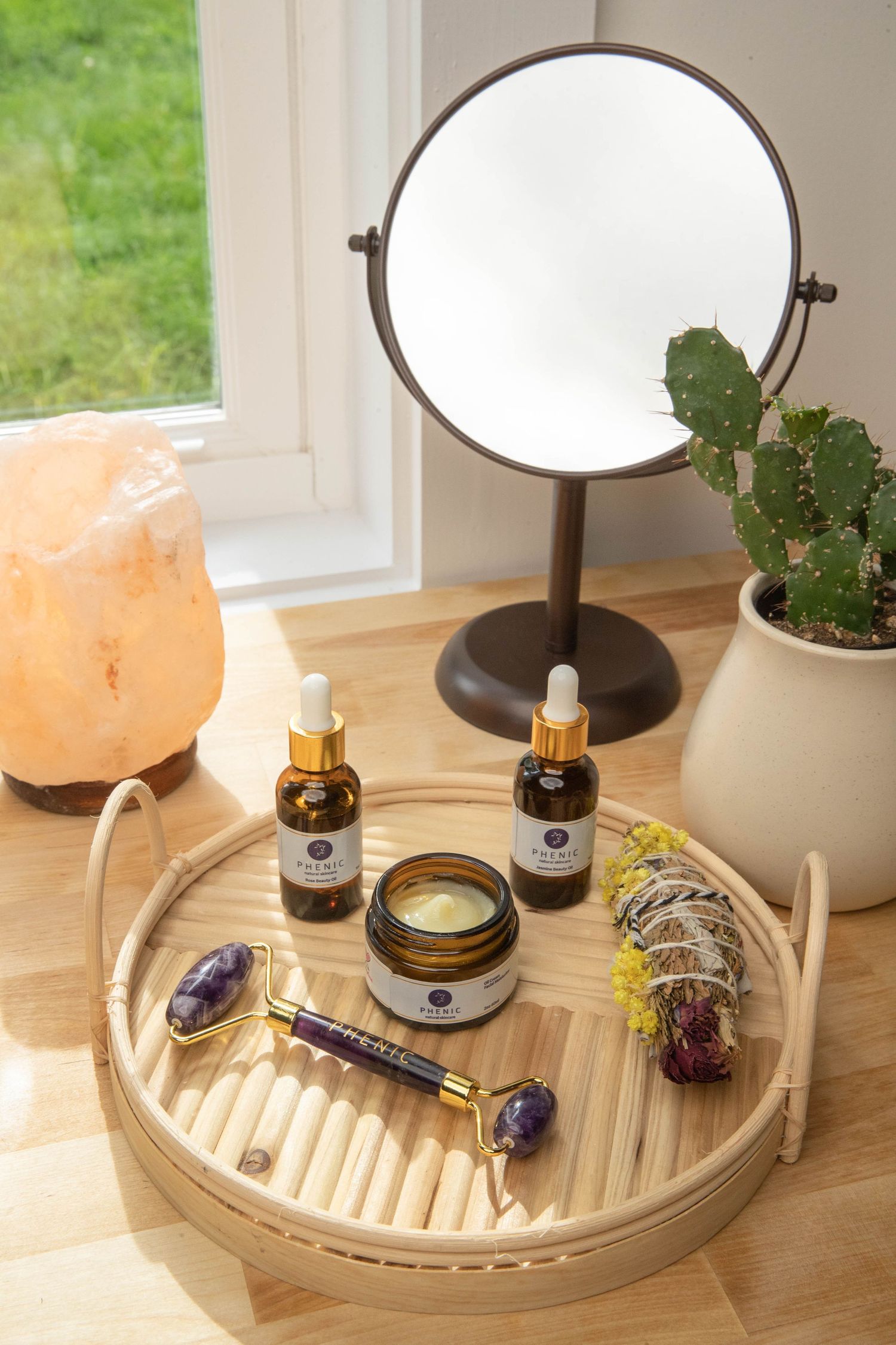 Wellness products arranged on wooden tray with mirror, salt lamp, and cactus plant.