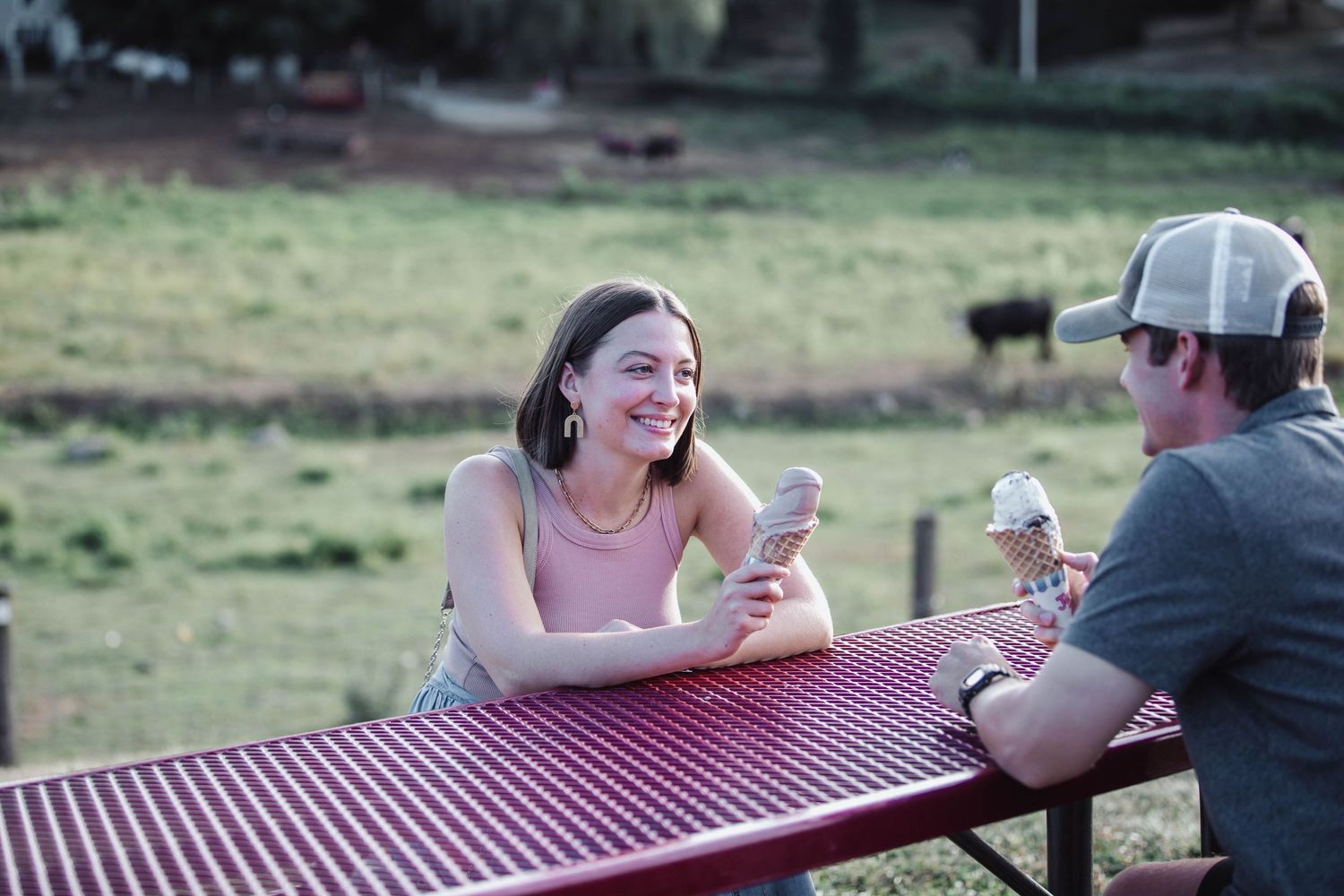 Two people enjoying ice cream and conversation at a red picnic table outdoors.