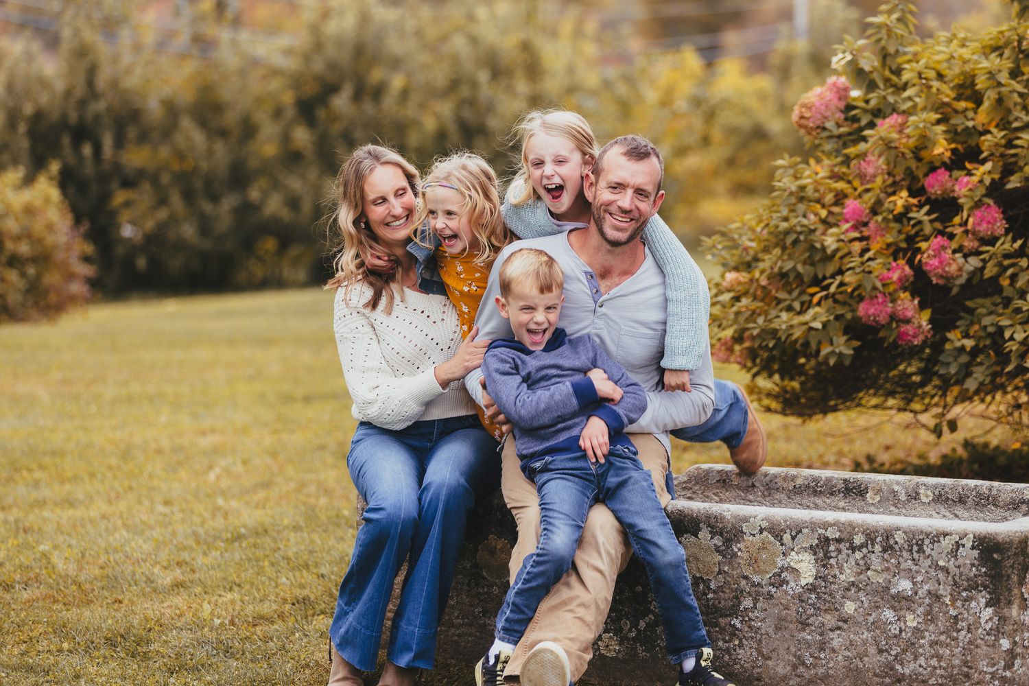 Candid outdoor family portrait on stone steps surrounded by autumn foliage.