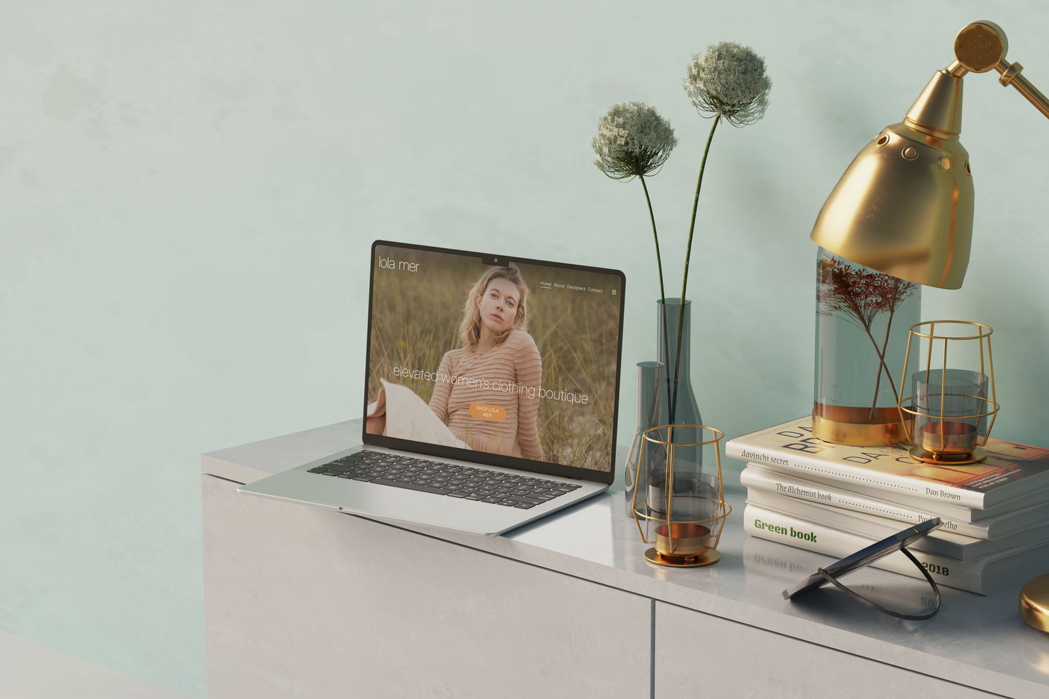 Minimalist home office setup with laptop, desk lamp, and glass jar on wooden desk against mint green wall.