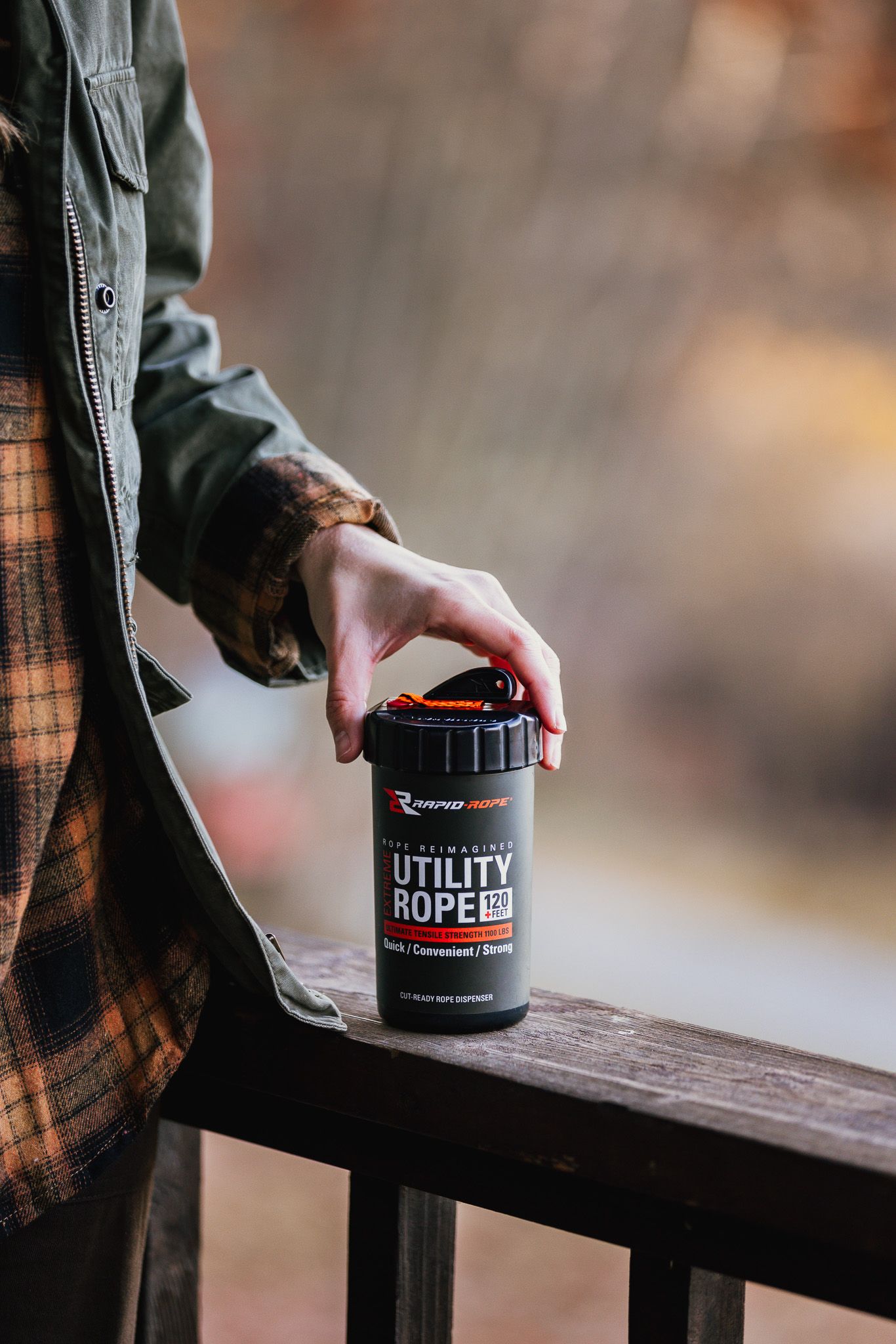 Hand placing a black utility rope container on wooden railing outdoors.