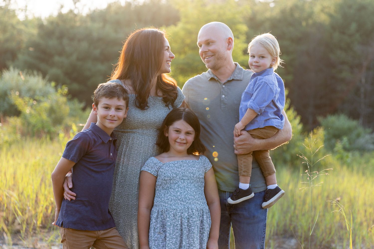 Family shares joyful moment together during sunset portrait session in field.