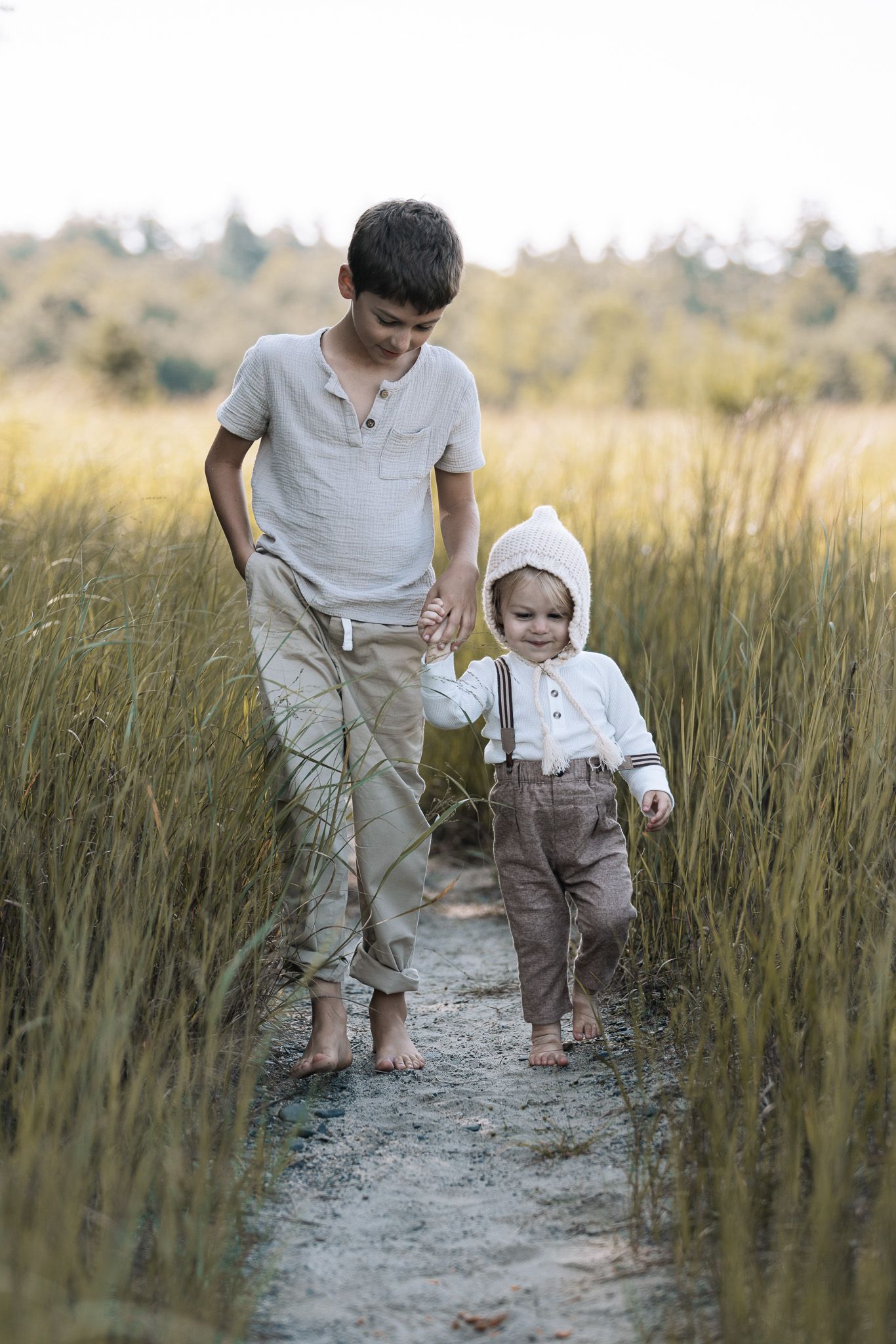 Children walking together on a dirt path through tall grass during golden hour.