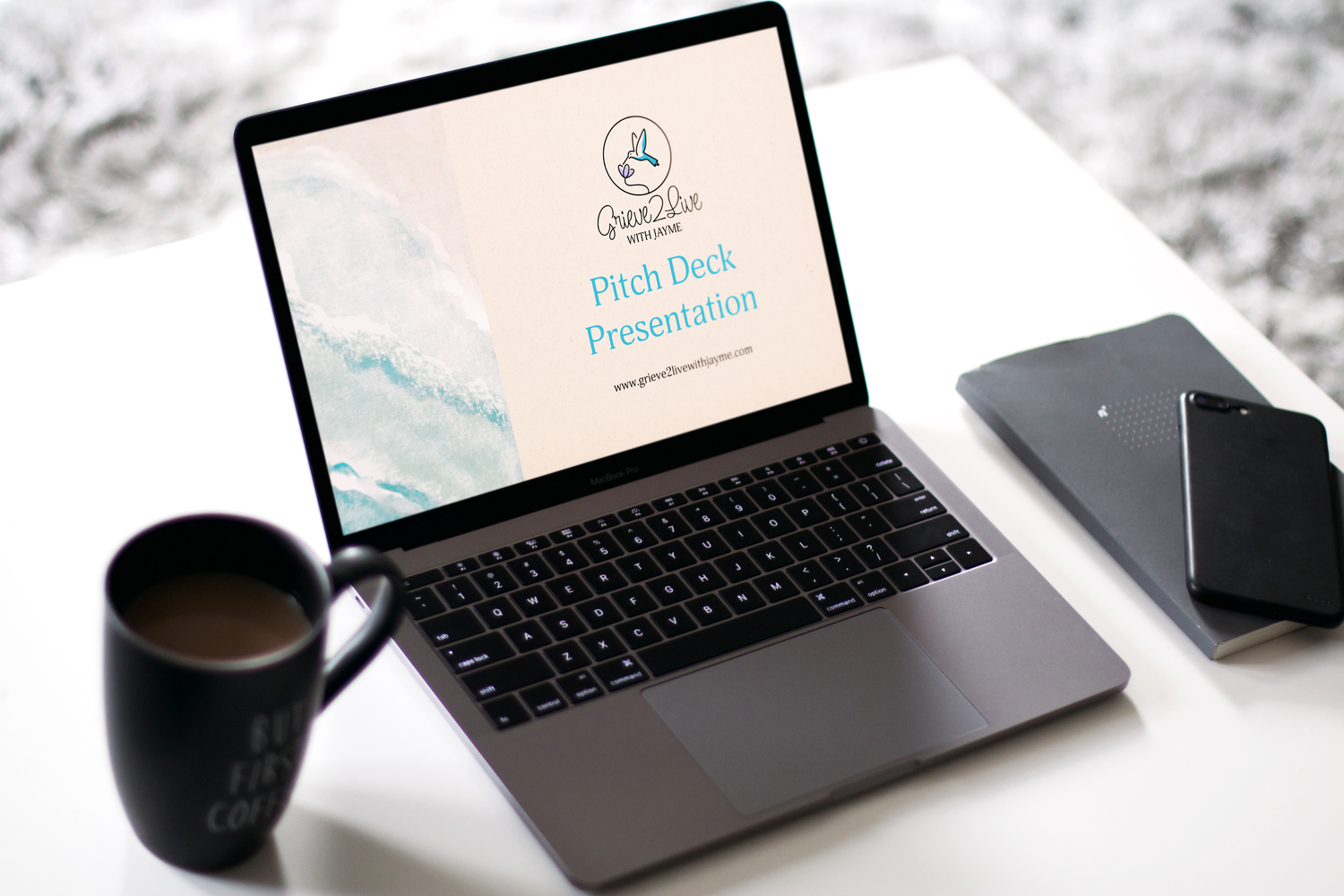 A black laptop computer with a minimalist workspace setup showing a mug and desk accessories.