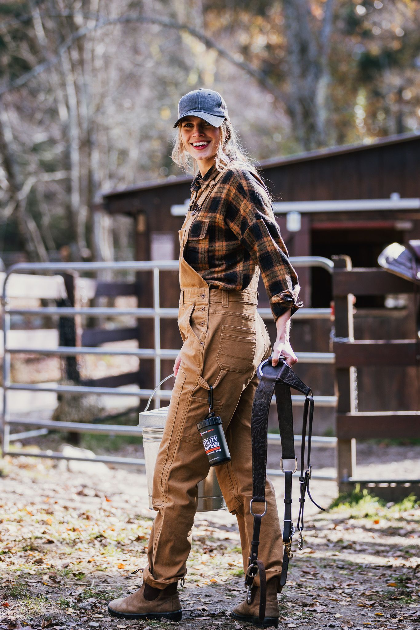 Person in workwear and baseball cap standing near wooden fence in autumn setting.