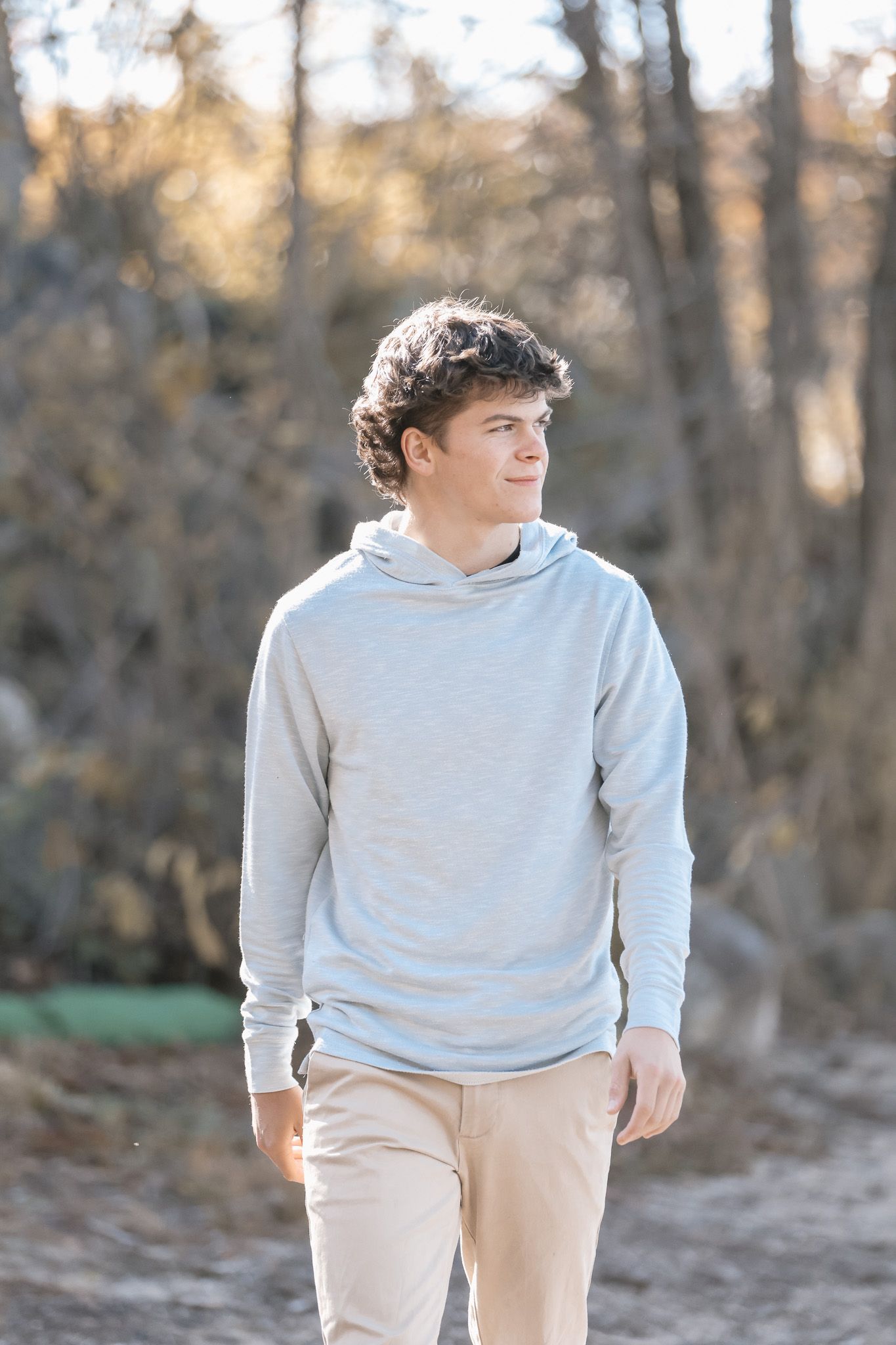 Teen walking outdoors in light gray hoodie and khaki pants during winter photoshoot.