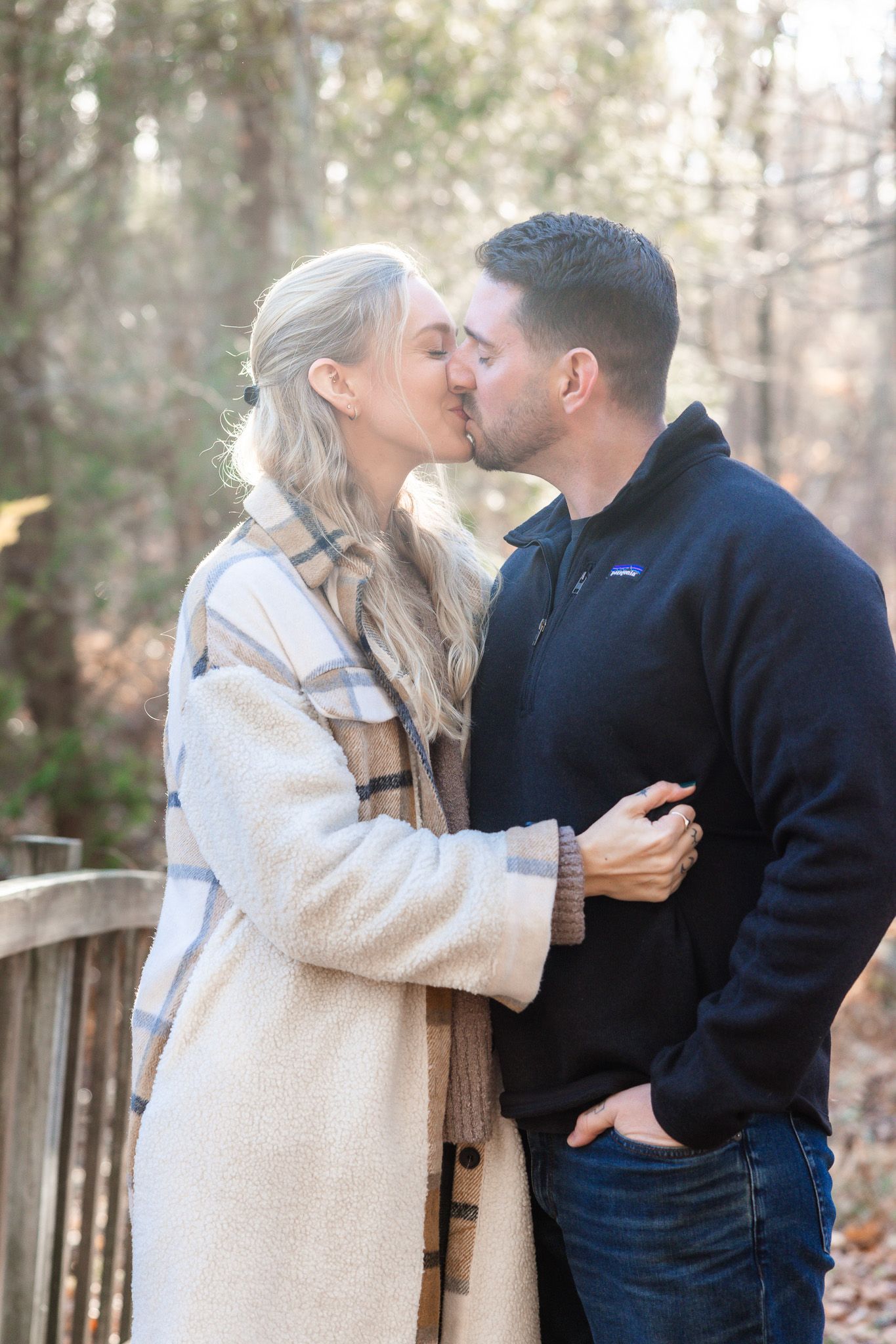 Couple sharing an intimate moment on a wooden deck surrounded by winter foliage.