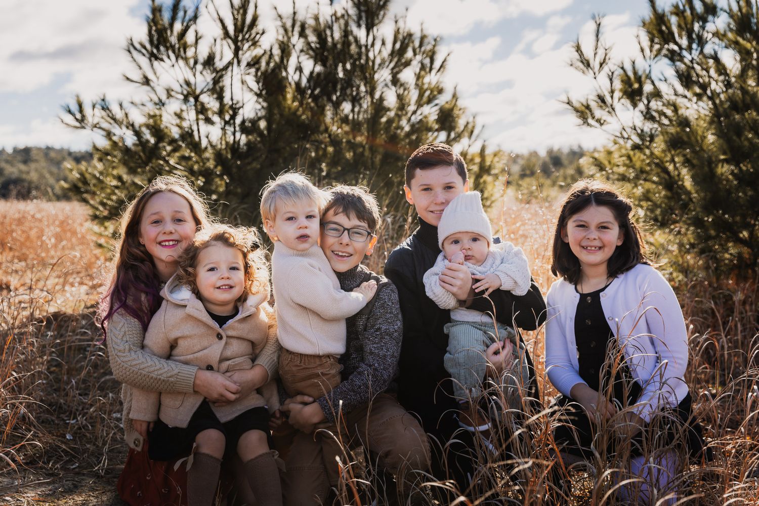 Casual family portrait outdoors with pine trees and golden sunlight.