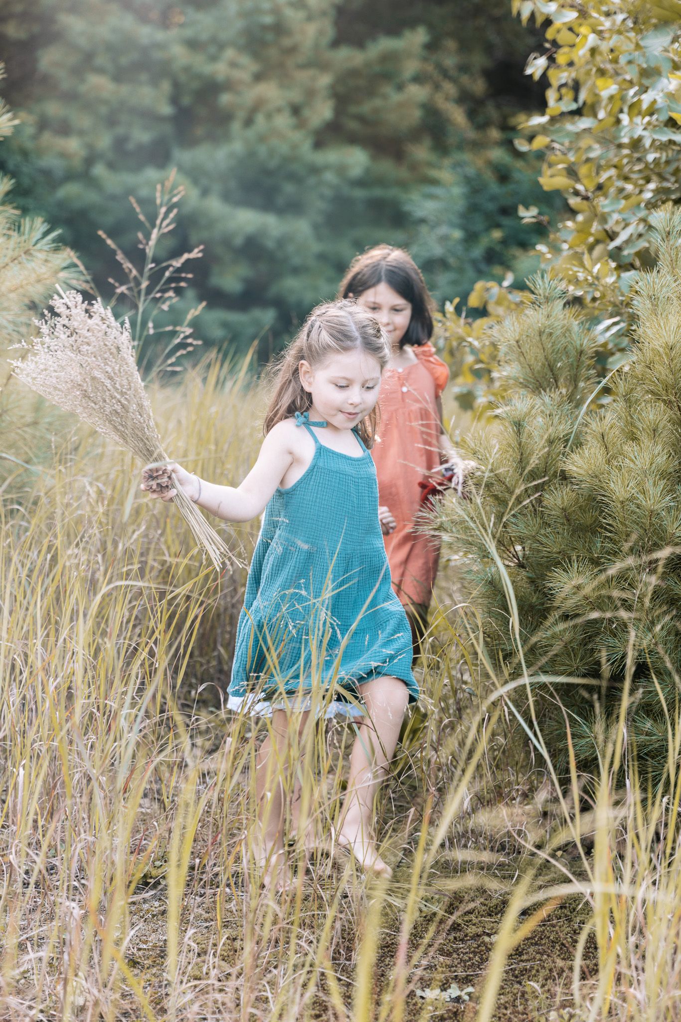 Children play among tall grasses in a natural setting during golden hour.