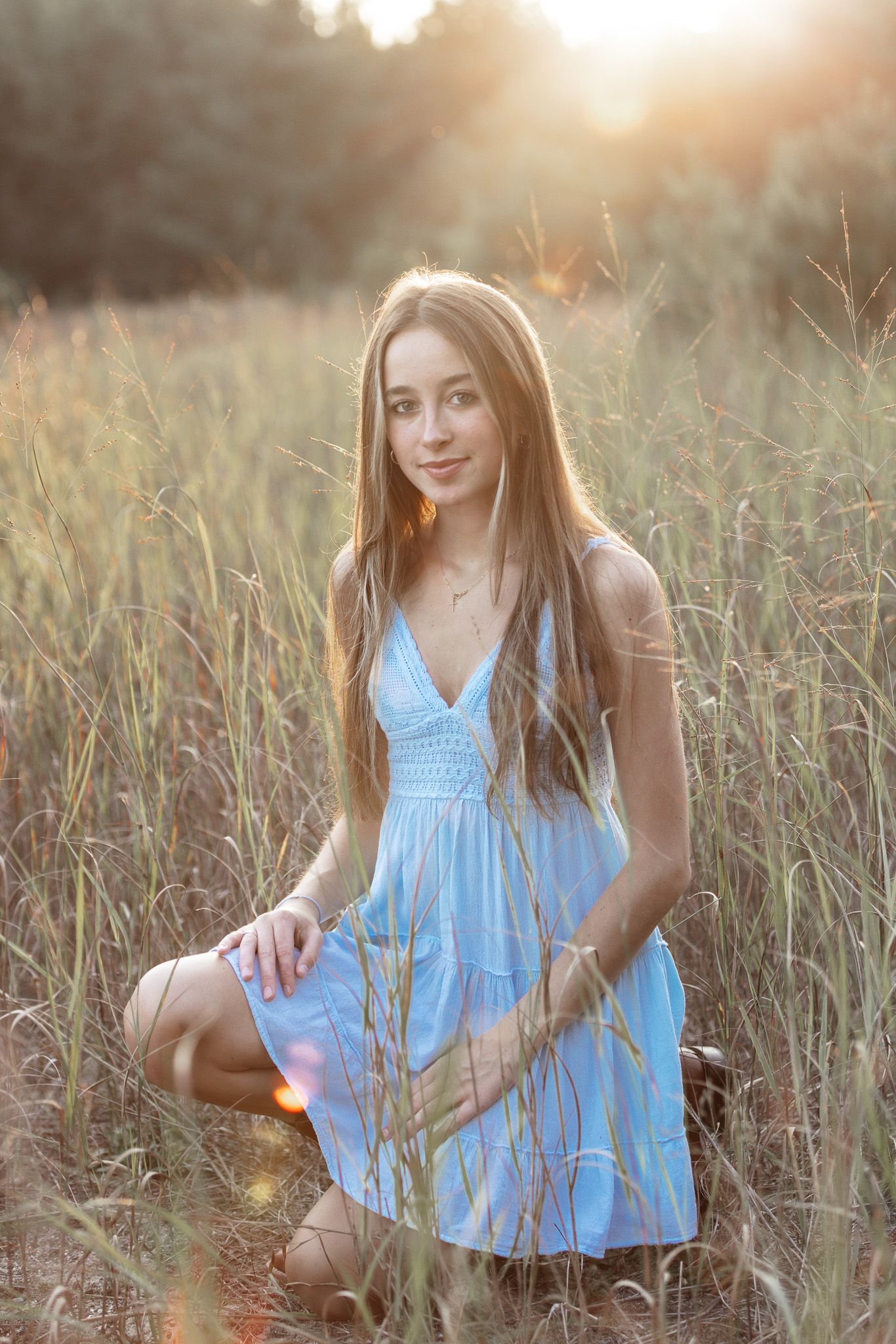 Person in light blue sundress sits among tall grass during golden hour photoshoot.