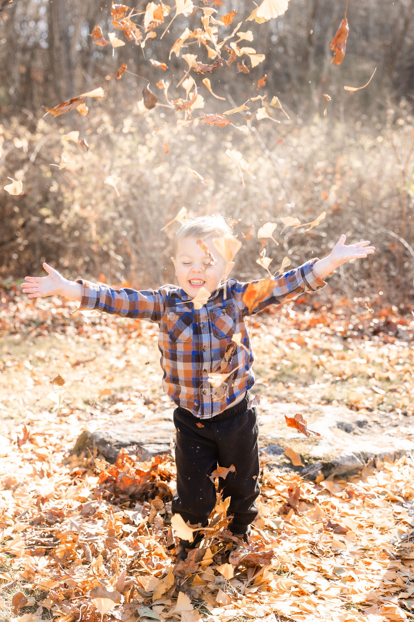 Child playing in fallen autumn leaves with orange and brown foliage flying through the air.