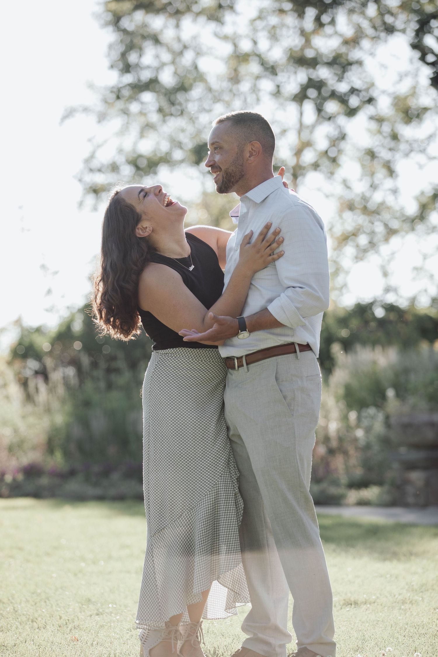 A couple dancing and embracing in a sunny outdoor field with trees in the background.