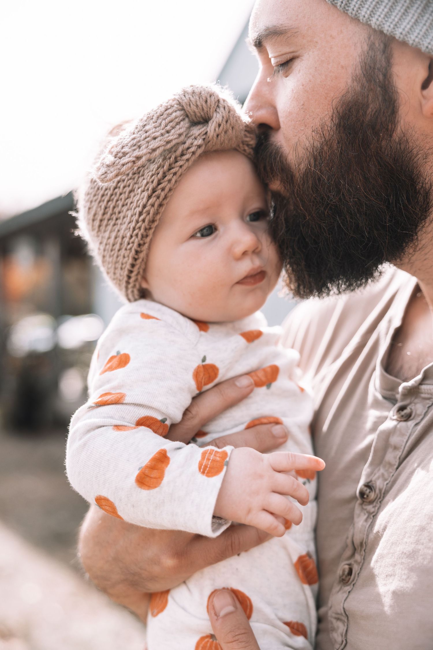 Baby in pumpkin print outfit and knit hat being held and kissed.
