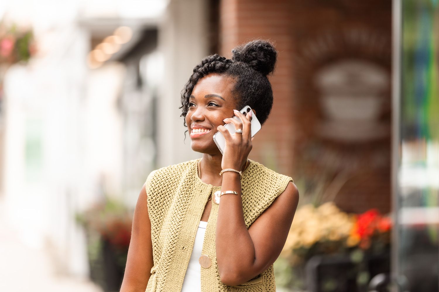A person in a yellow vest talks on phone while walking down a city sidewalk.
