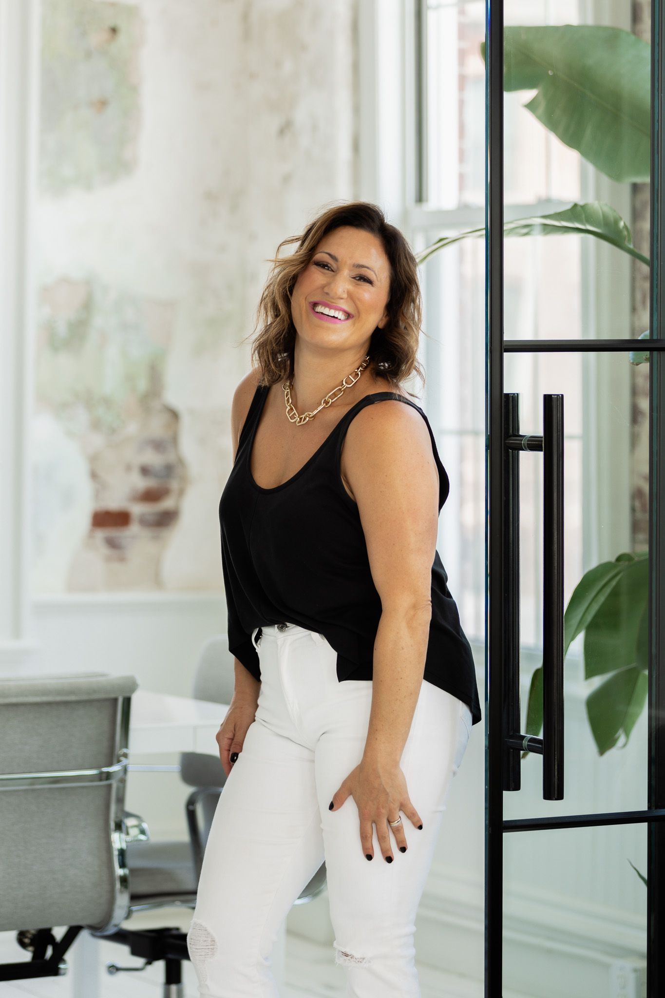 Person in black top and white pants posing confidently in modern office space.