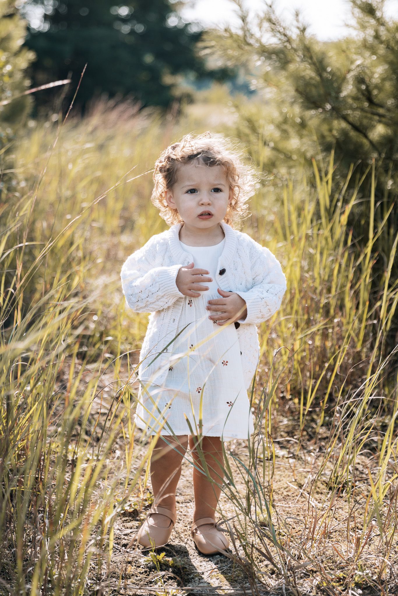 A small child explores a natural setting wearing a white embroidered dress.