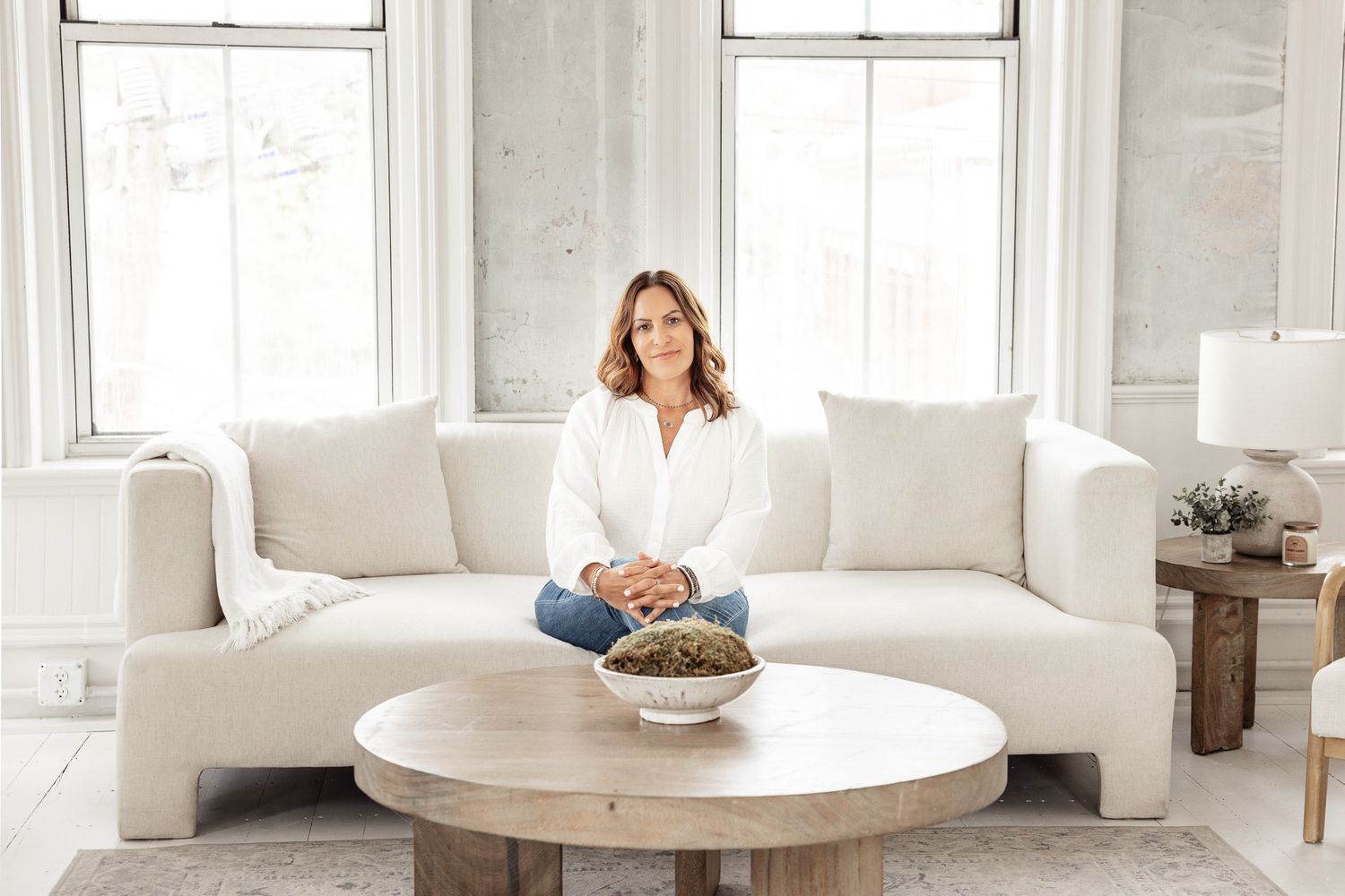 A bright white living room features a curved sofa, round coffee table and natural decor in a modern coastal style.