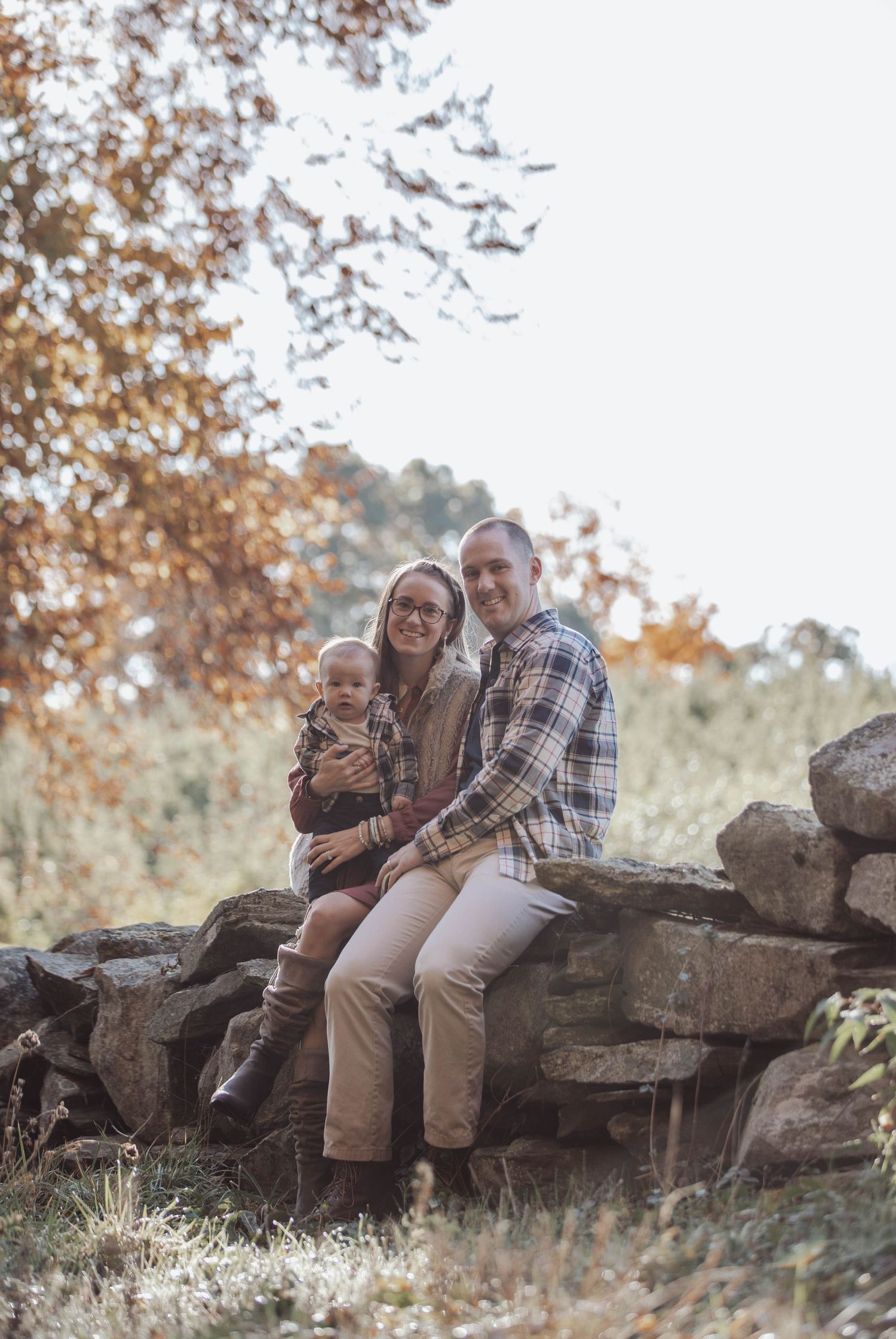 A family sits together on a stone wall surrounded by fall foliage.