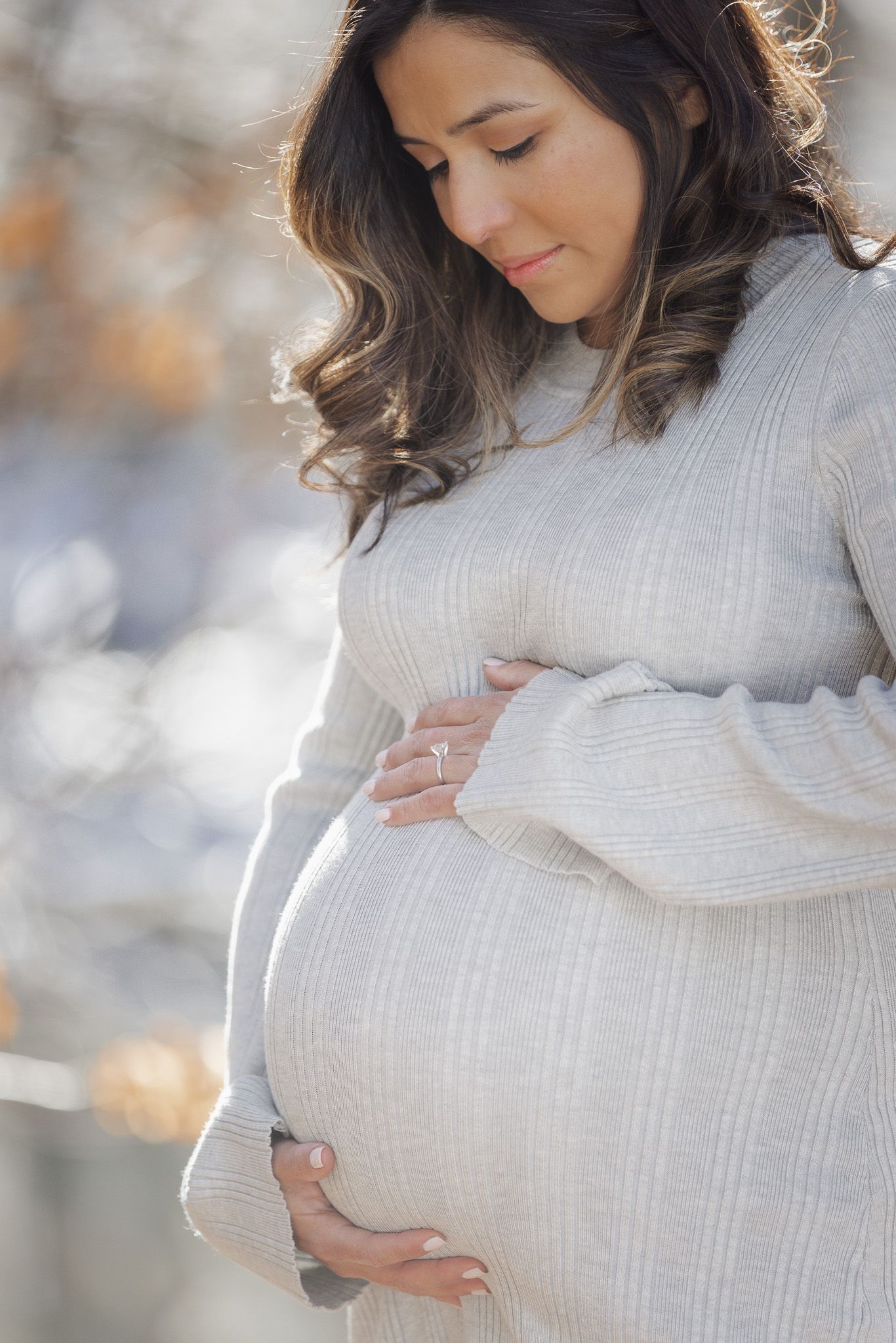 Woman in white sweater holding her pregnant belly in soft winter light.