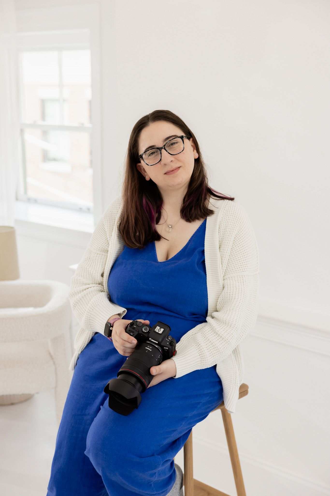 Indoor studio portraits with camera in bright white space wearing blue dress.